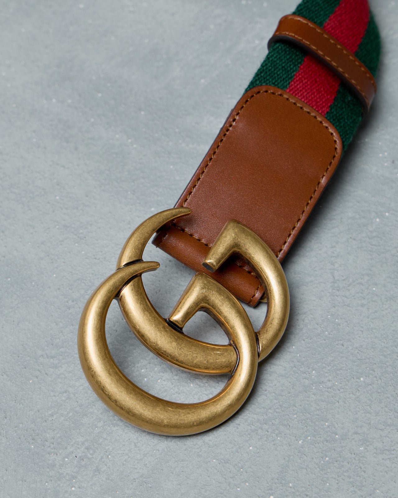Gucci belt with green and red striped strap and brown leather buckle on a gray background