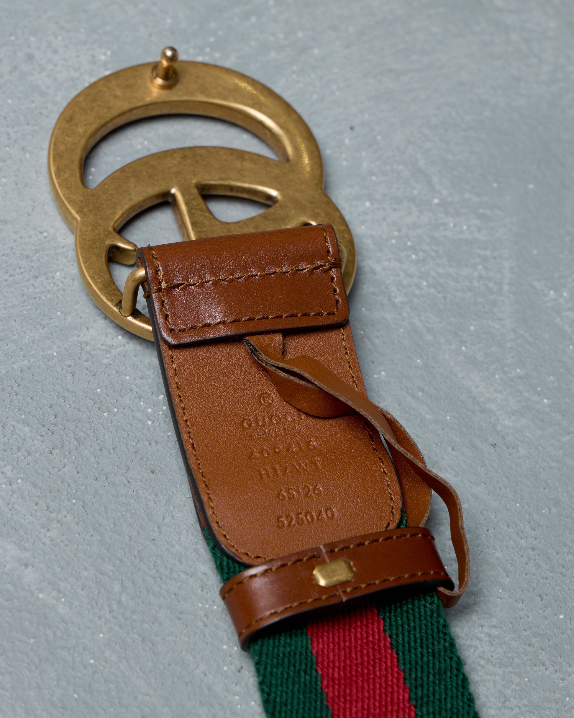 Gucci brass belt buckle with brown leather strap and green and red webbing on a gray background