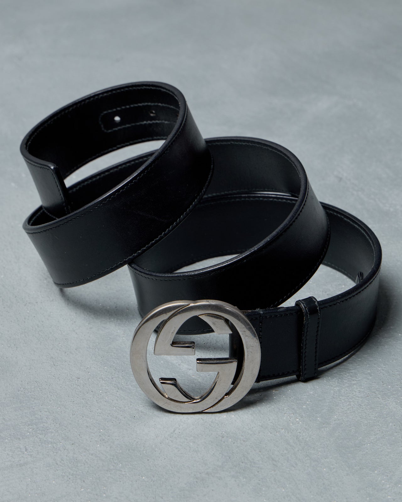 Black leather Gucci belt with a silver buckle on a gray background