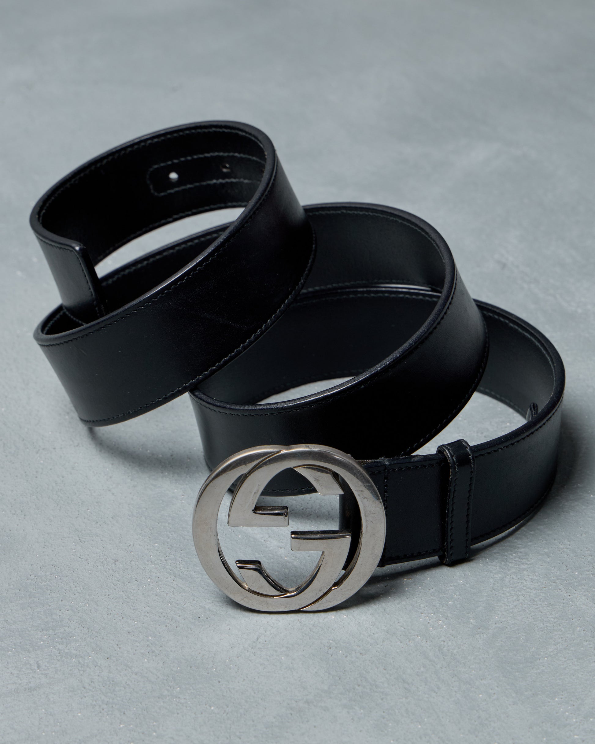 Black leather Gucci belt with a silver buckle on a gray background