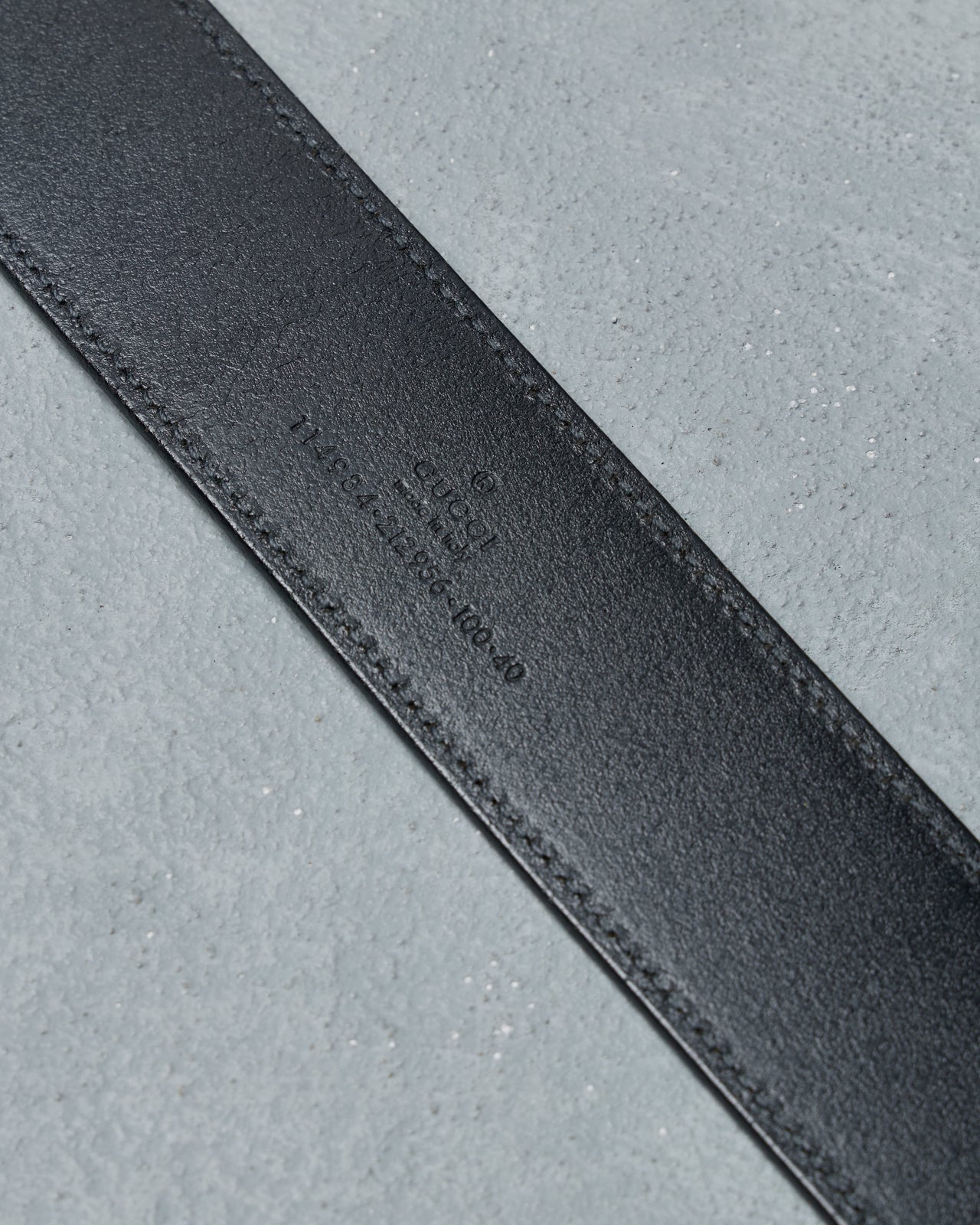 Black leather Gucci belt with a silver buckle on a gray background