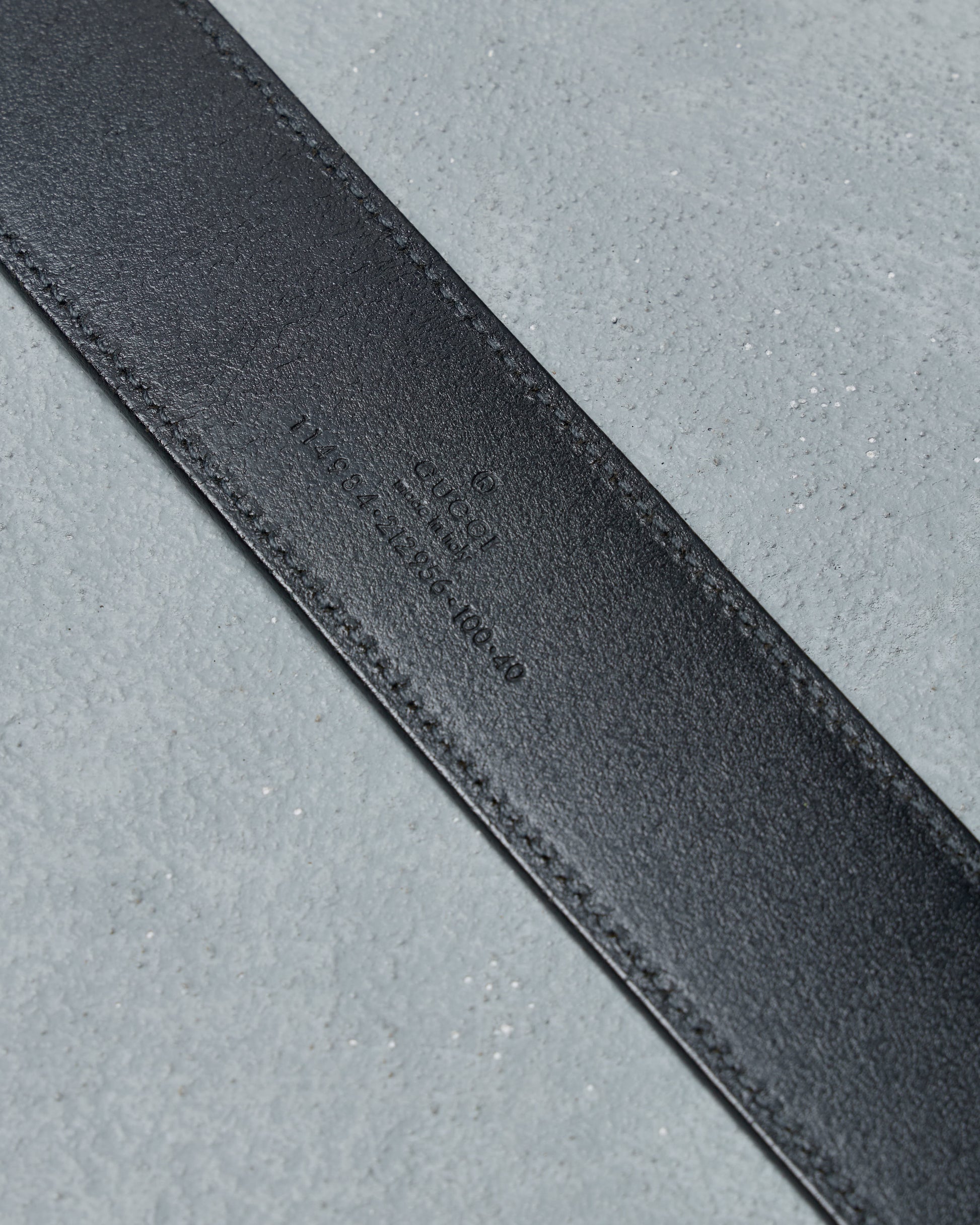 Close-up of a black leather Gucci belt  strap on a gray background