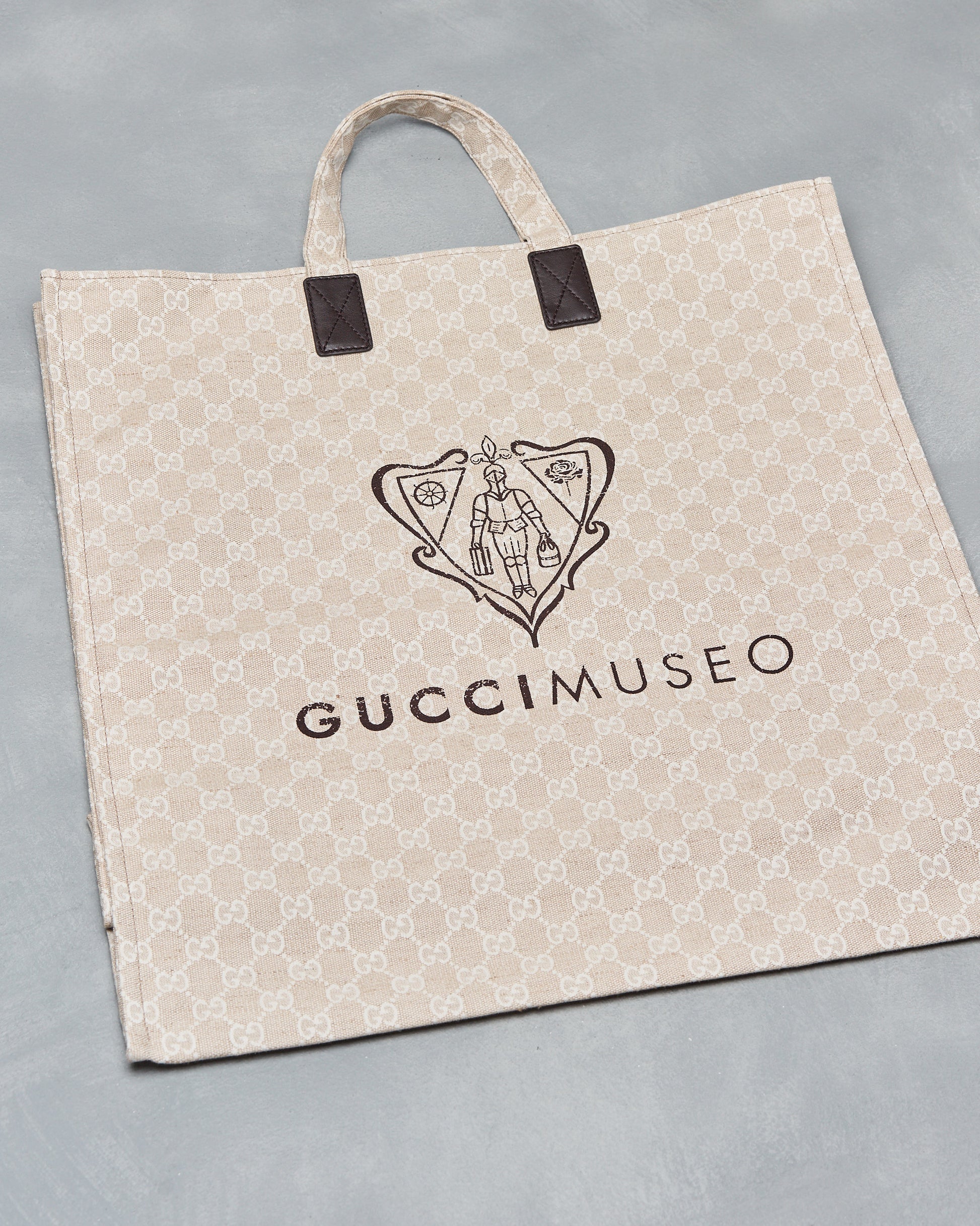 A beige Gucci GG Museo canvas shopper tote bag with a printed design on the face, canvas handle with leather reinforcement, and the Gucci brand logo on the side.