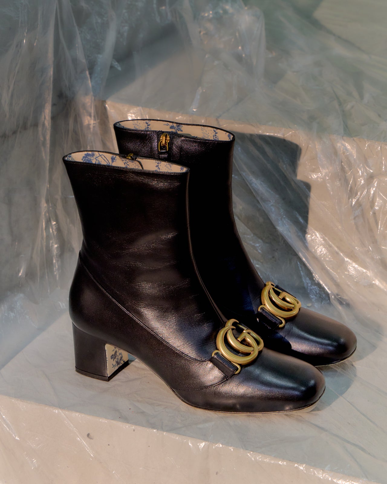 Pair of black leather Gucci boots with gold logo on a white surface