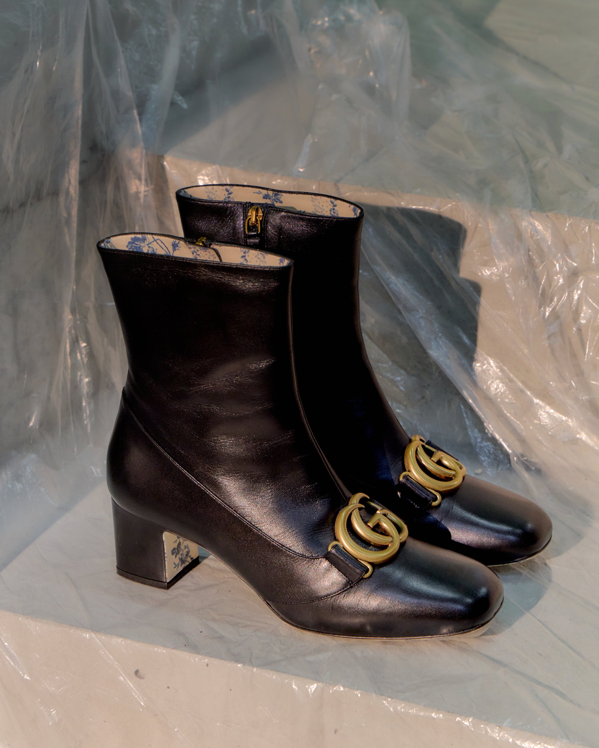 Pair of black leather Gucci boots with gold logo on a white surface