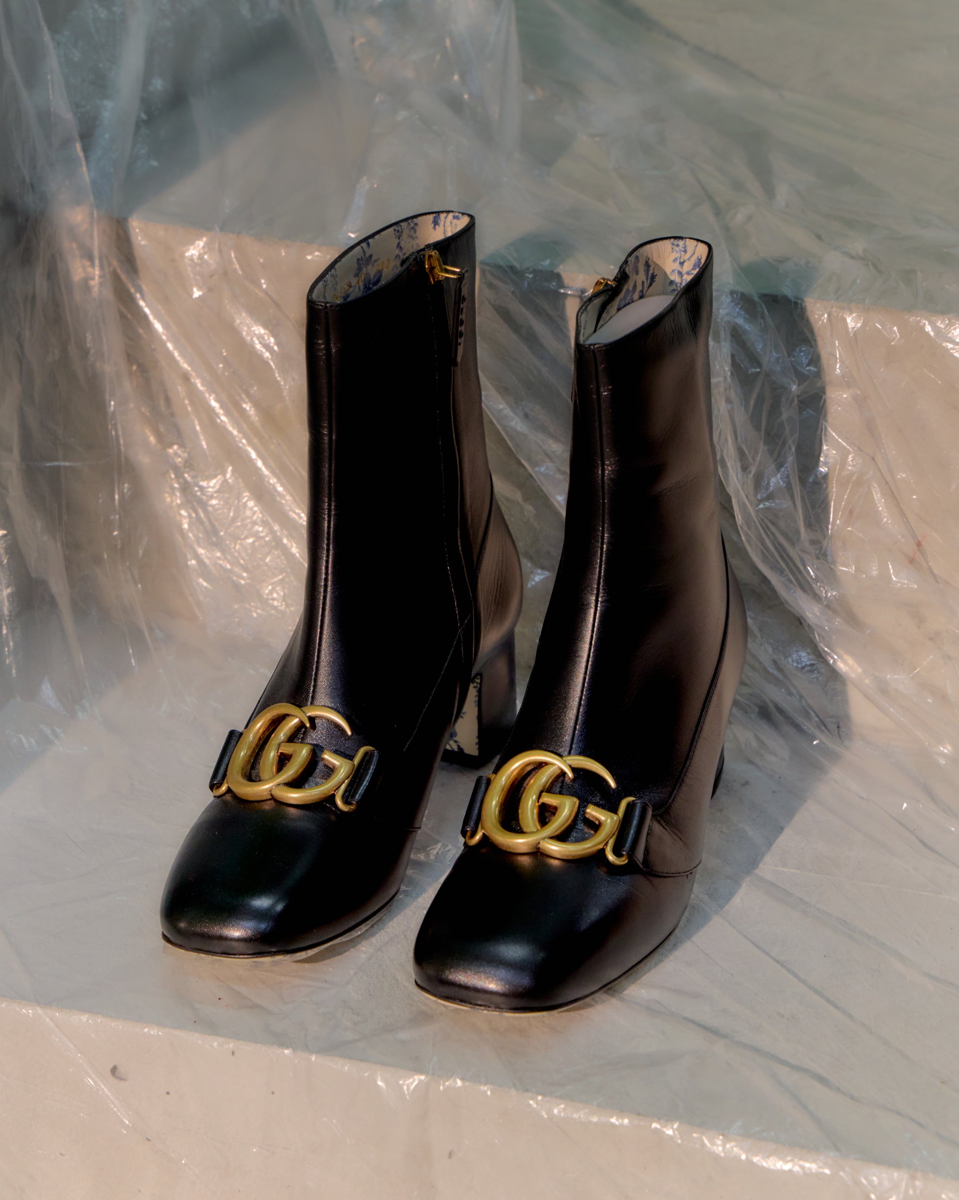 Black Gucci boots with gold buckles on a reflective surface