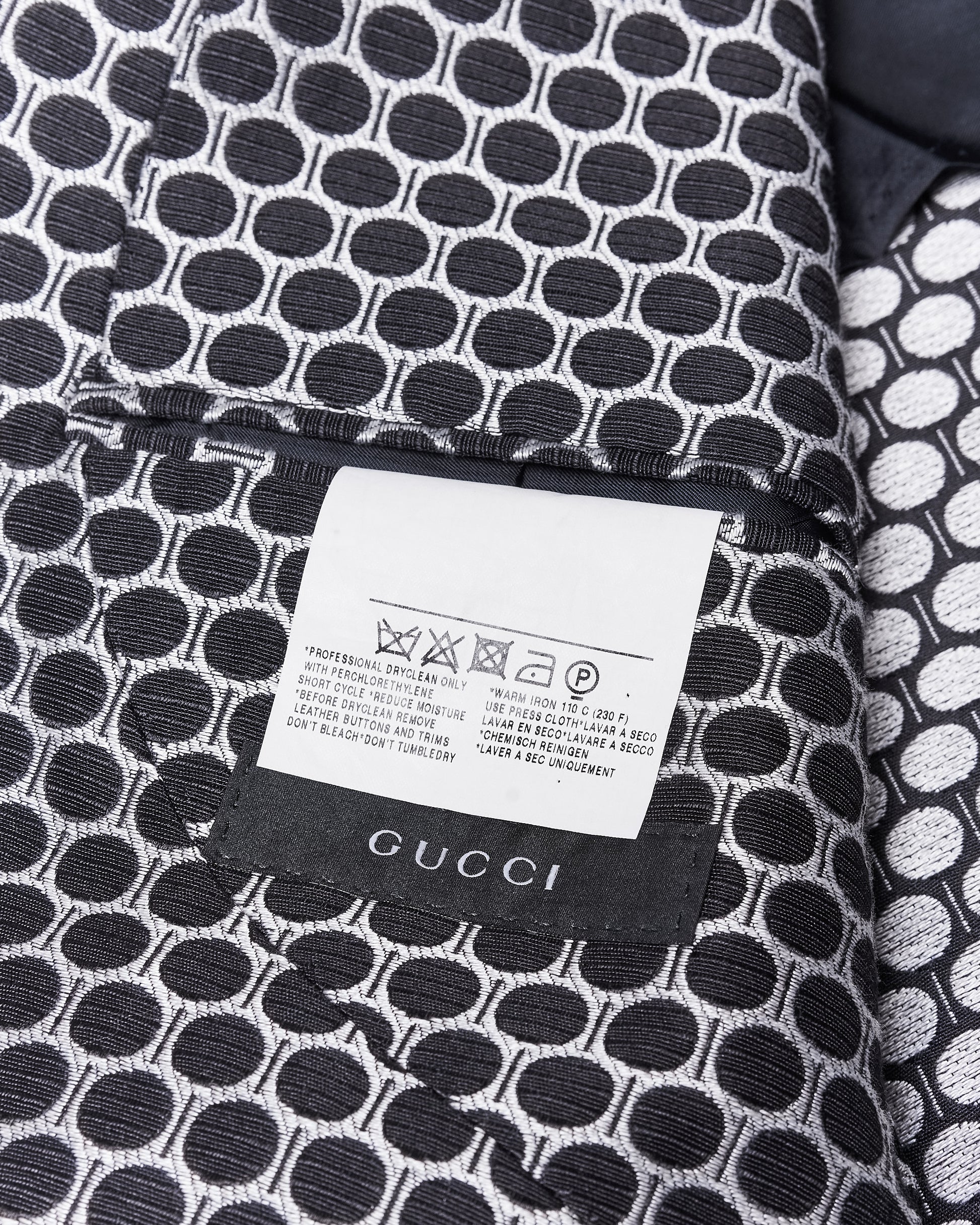Close-up of a black and white patterned fabric with circular shapes. A label displays the Gucci logo and dry cleaning instructions.