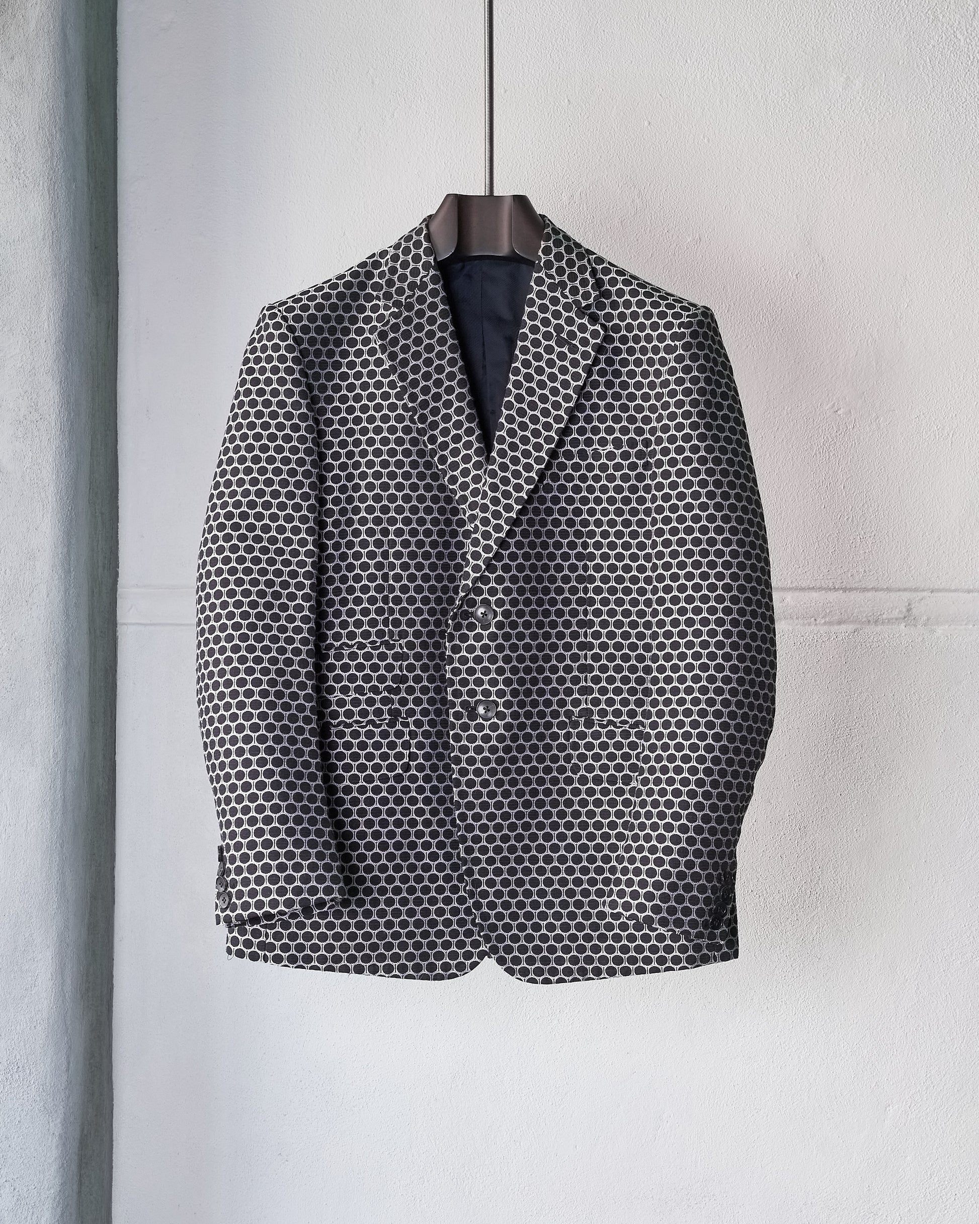 Grey and white polka dot Gucci blazer hanging against a light grey wall. 