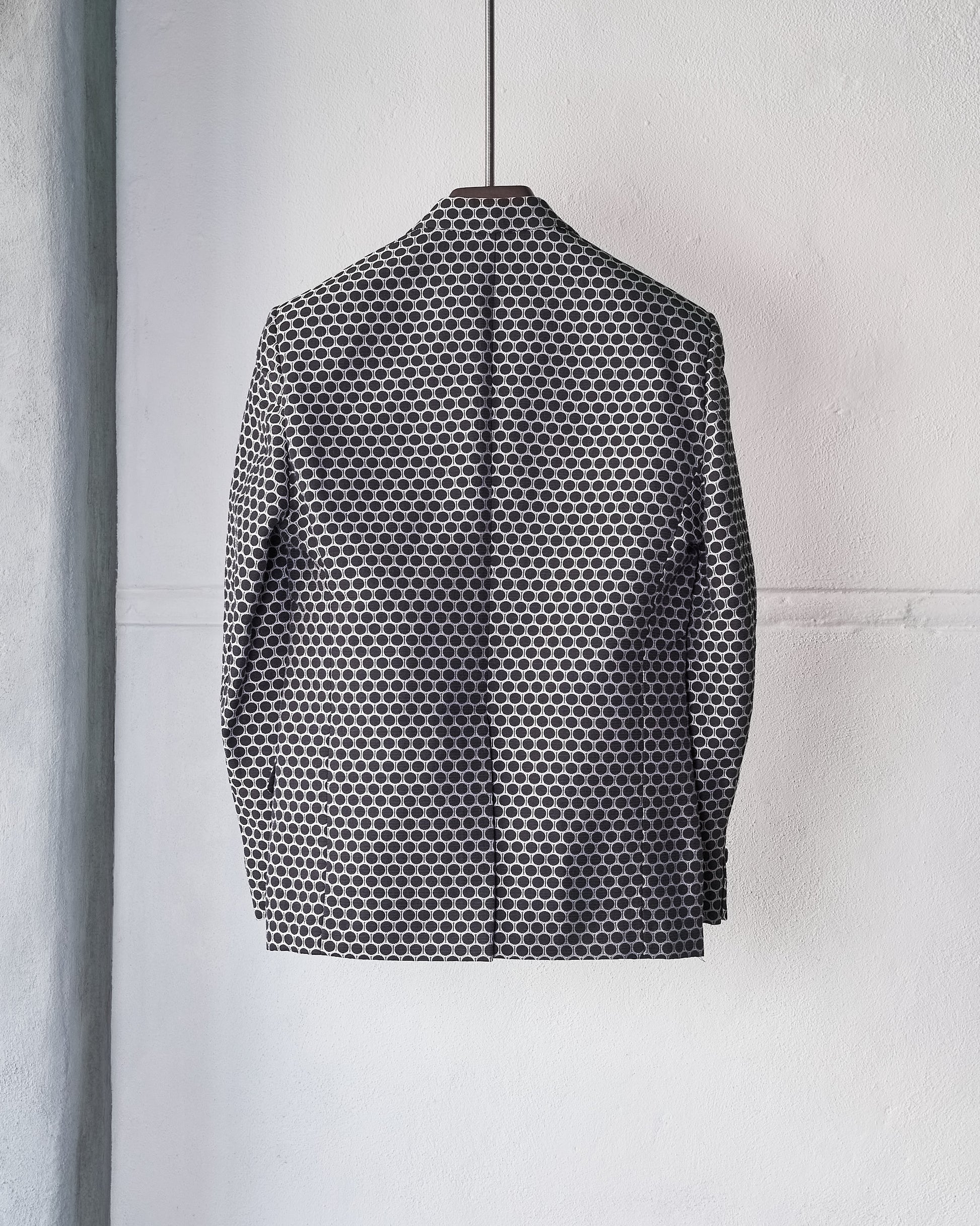 A black and white polka dot Gucci by Tom Ford suit jacket hangs on a wall.