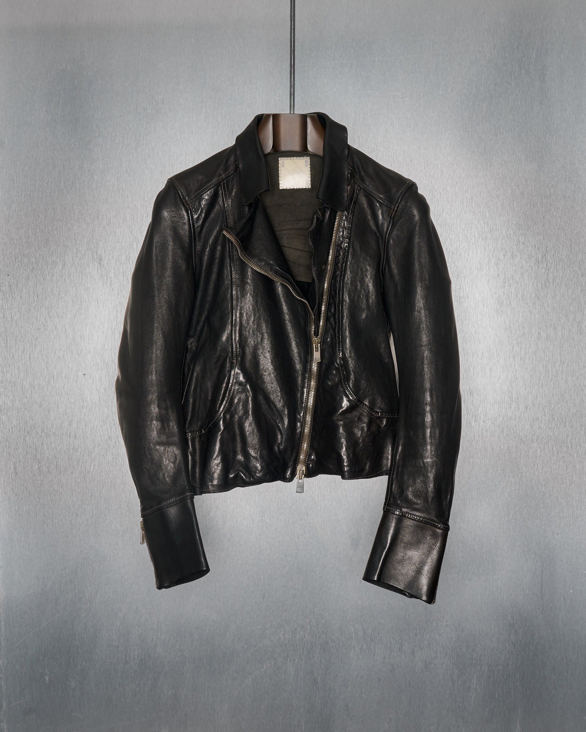 A black leather Guidi biker jacket with a satin sanded grain, featuring a diagonal double-zip front, two front pockets, and zip cordovan cuffs.