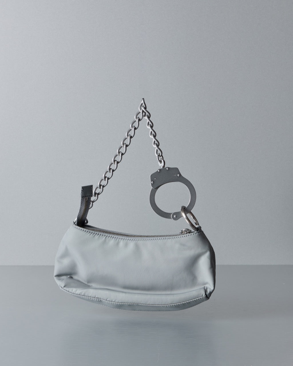 Silver Marc Jacobs handbag with a chain and handcuff detail on a gray background