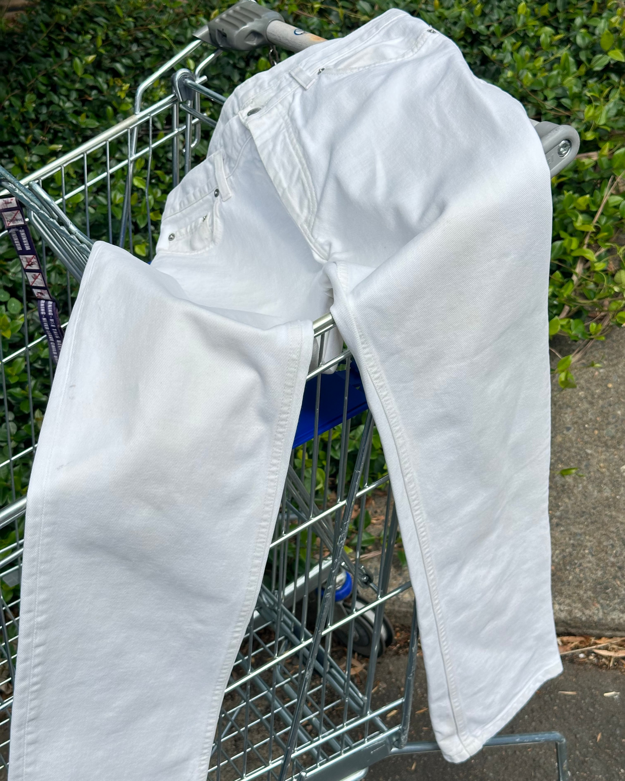 White Helmut Lang jeans draped over a shopping cart with a blurred background