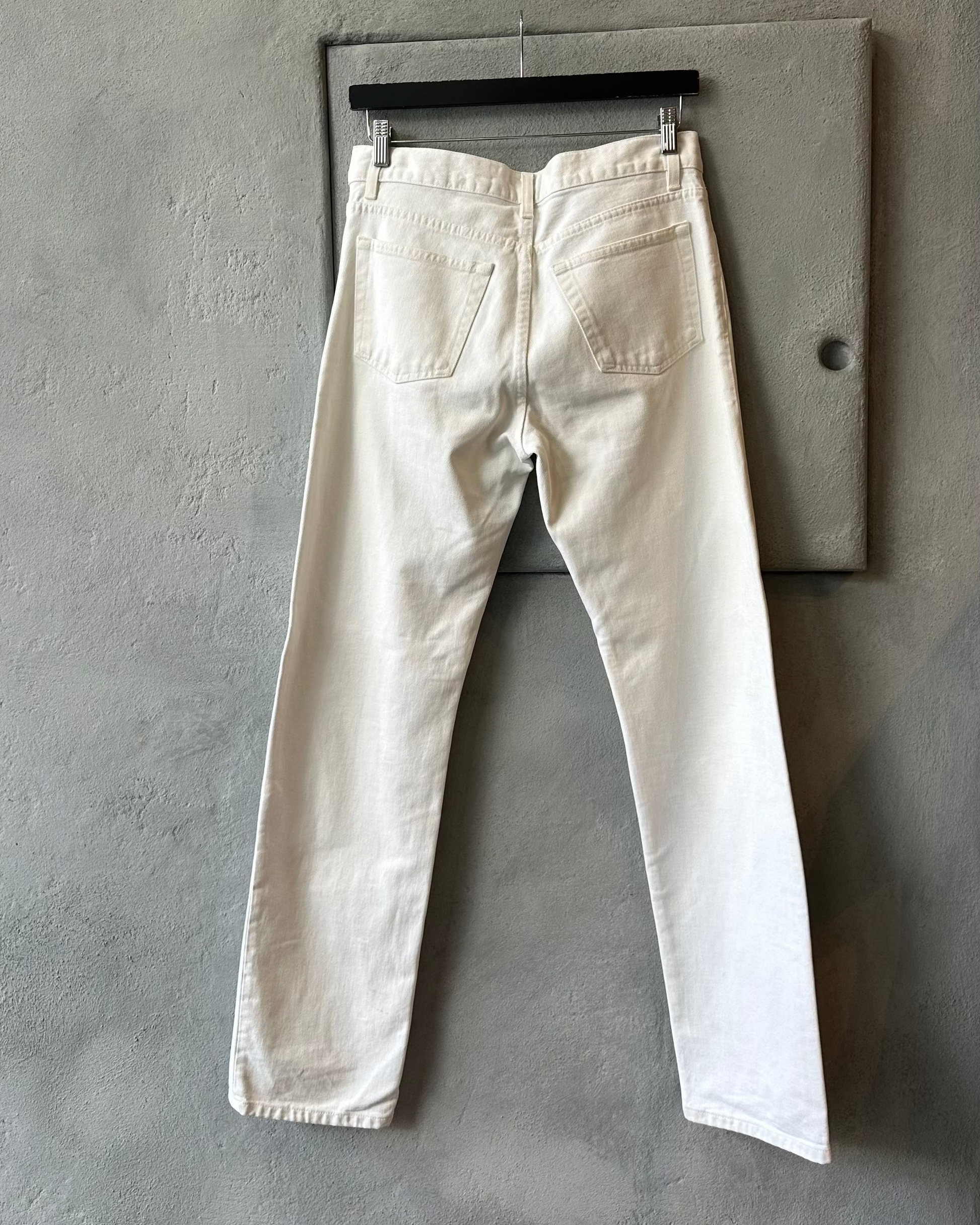 White Helmut Lang jeans hanging on a gray wall