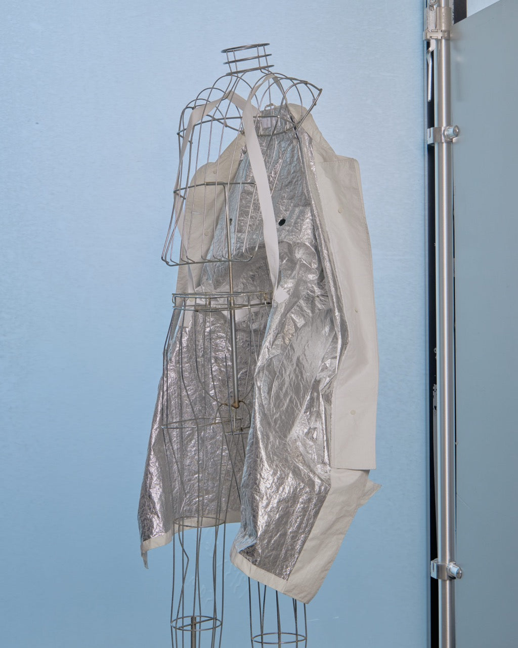 Mannequin with a silver metallic Helmut Lang jacket against a light blue wall