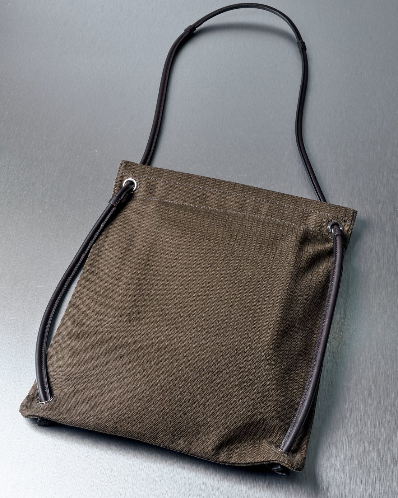 Olive green Hermes bag with black text "Hermes Sellier Paris" on the front, featuring black rope handles and a minimalist design on a metallic surface.