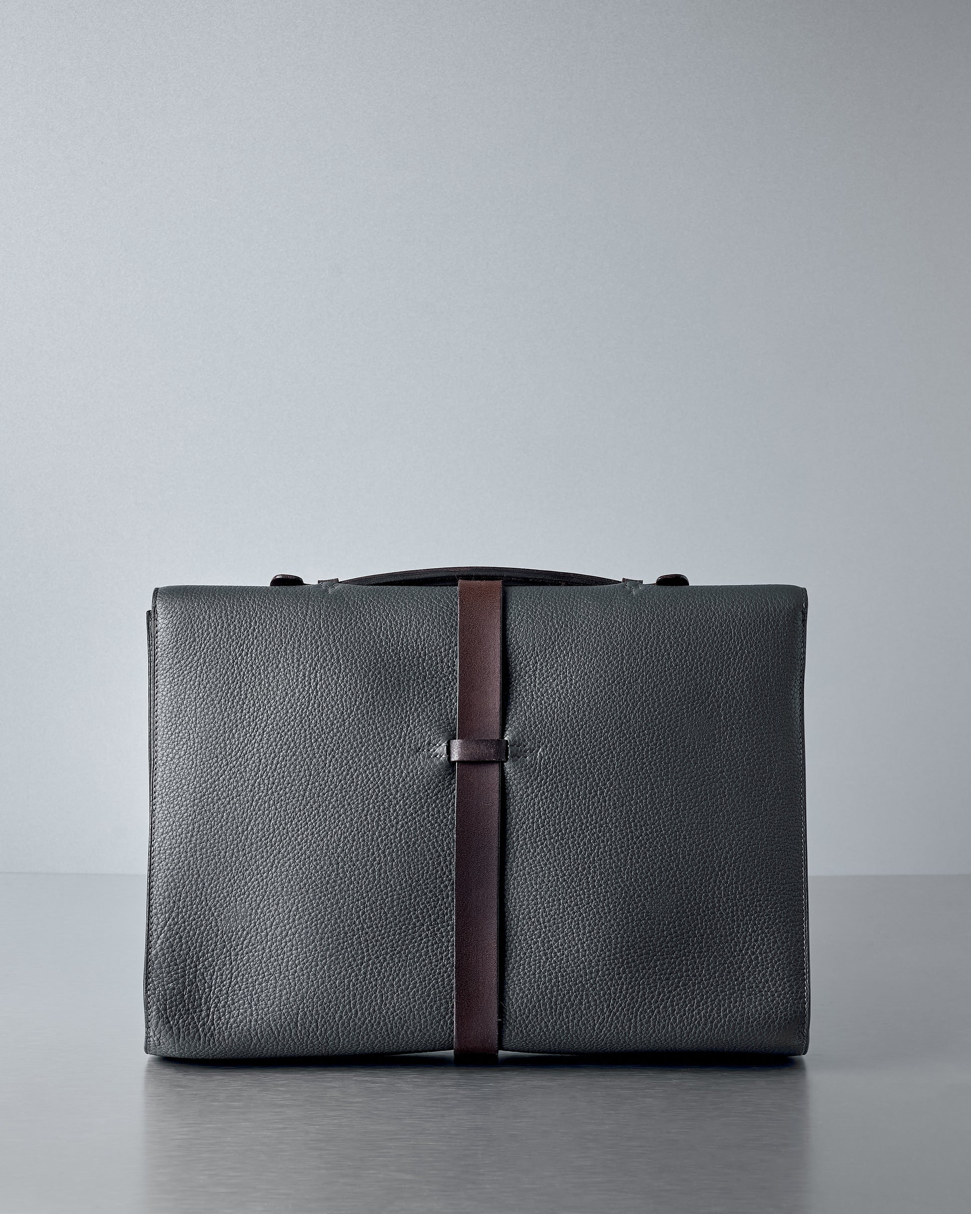 Indigo leather Hermès briefcase with a brown strap on a grey background