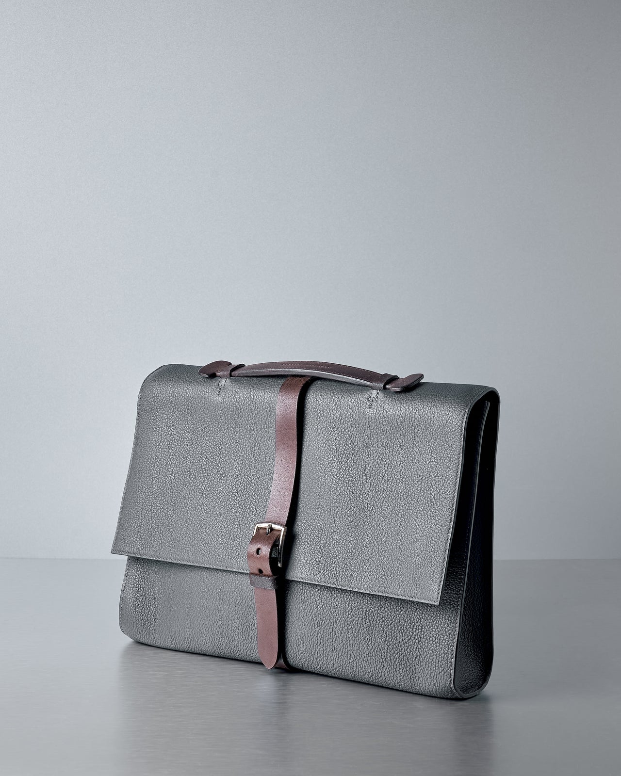 Indigo Hermès leather briefcase with a brown strap on a light grey background.