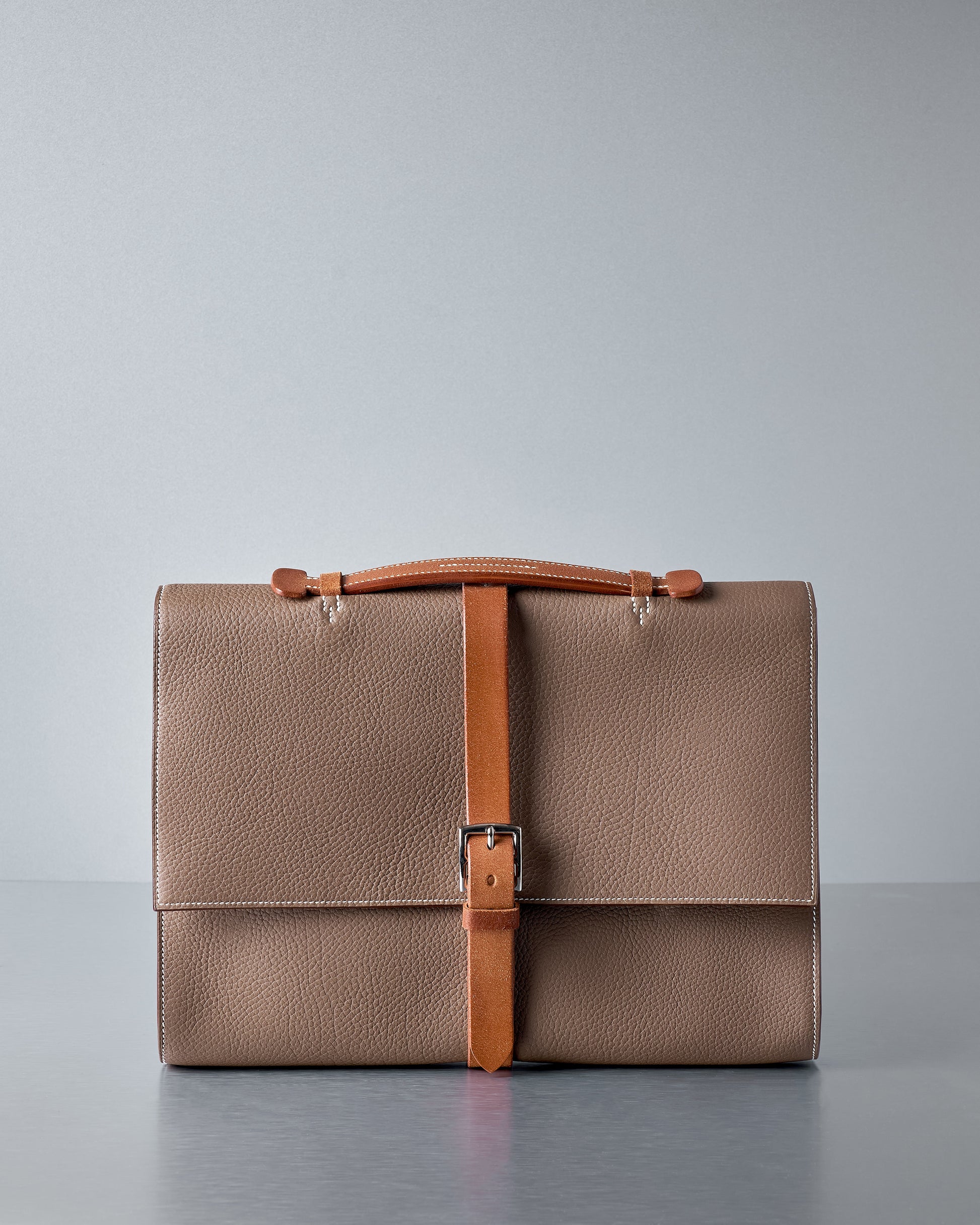 Brown leather Hermès briefcase with a strap on a grey background.