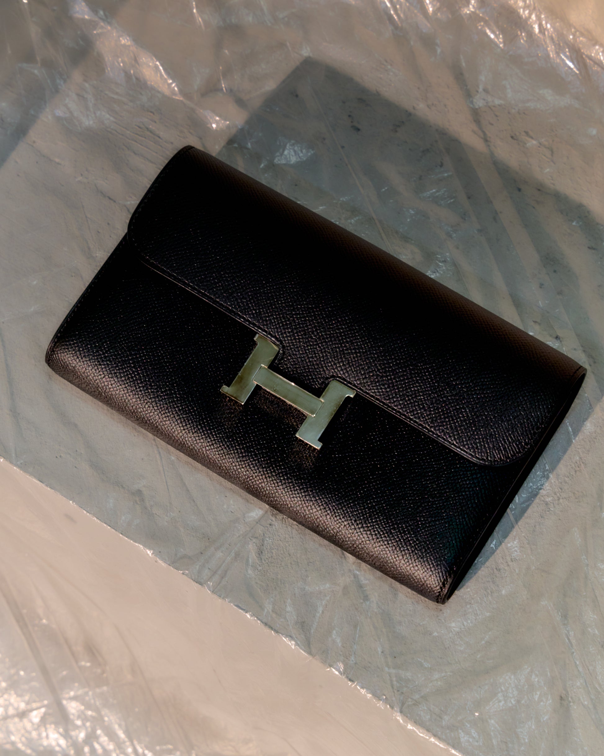 Black Hermès wallet with a gold 'H' logo on a reflective surface