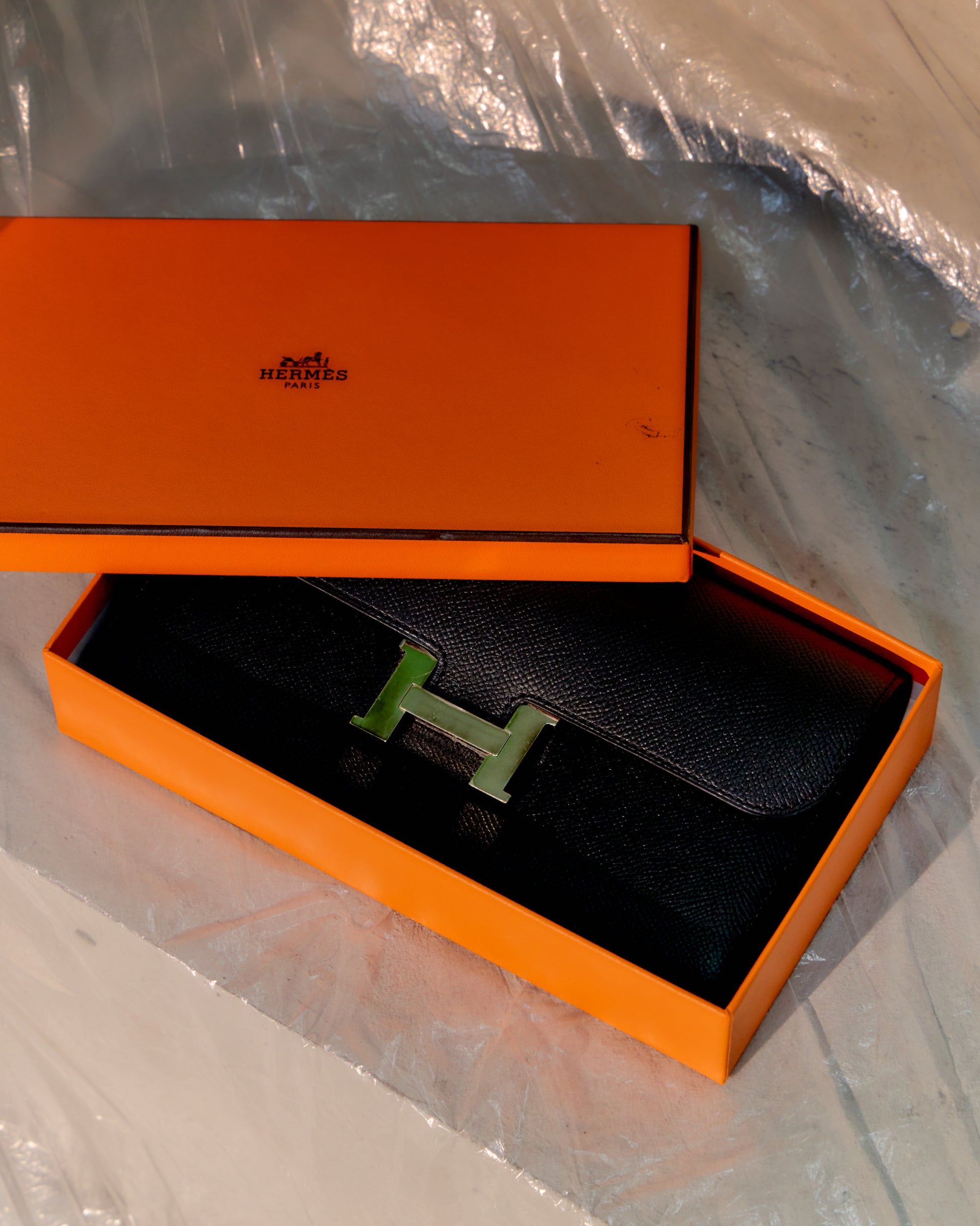 Hermès wallet in an orange box on a reflective surface