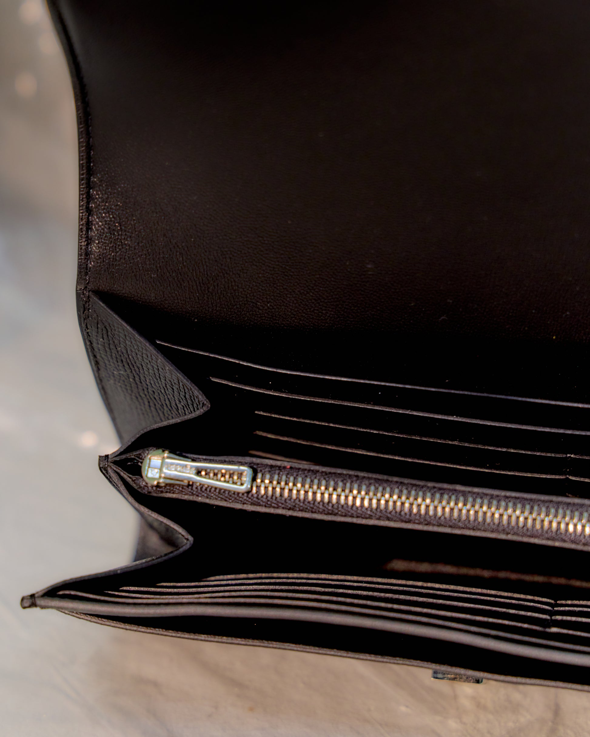 Close-up of a black leather Hermès wallet with a zipper on a light grey background