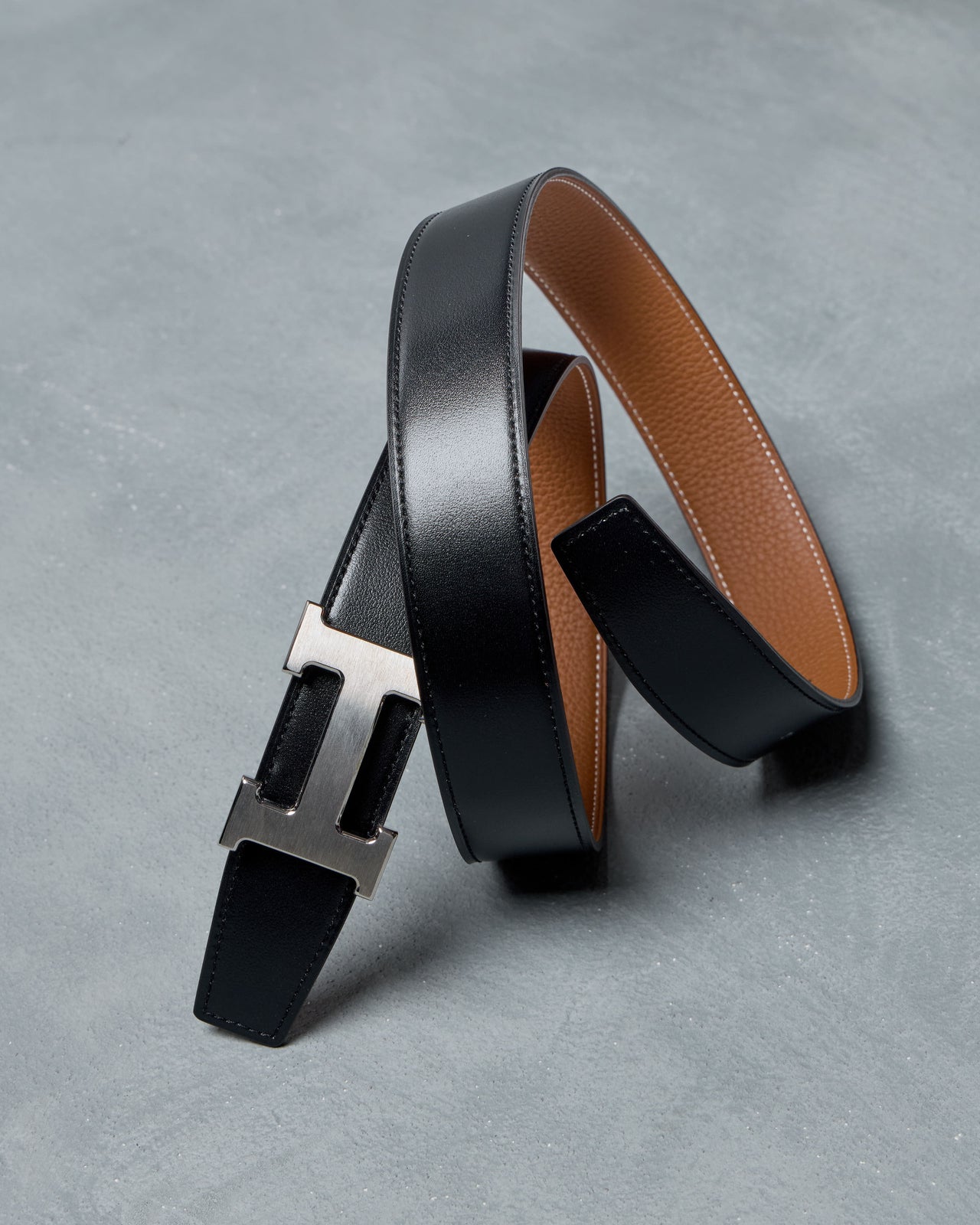 Black leather Hermes belt with a silver buckle on a gray surface