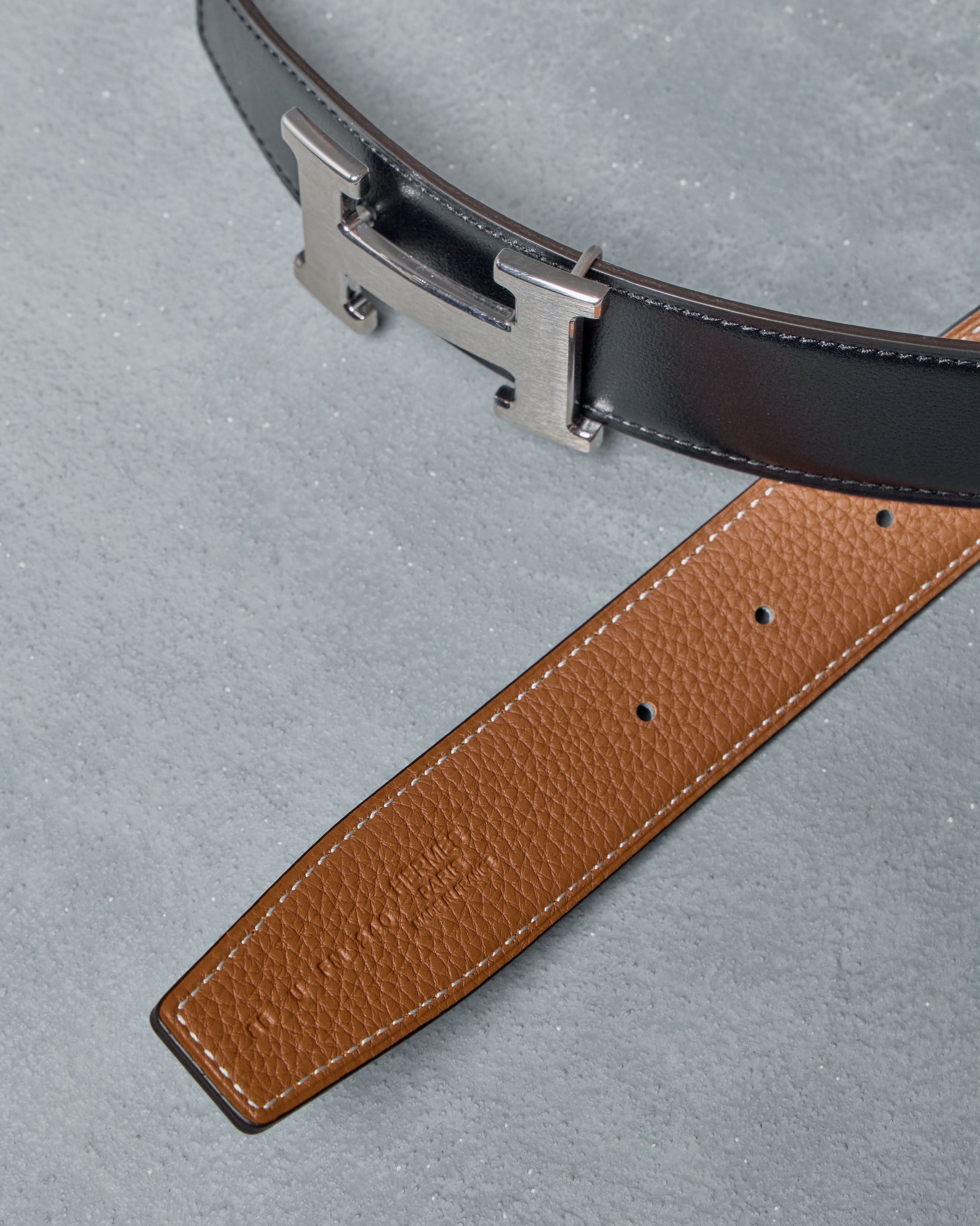 Brown leather Hermes belt with silver buckle on a gray background