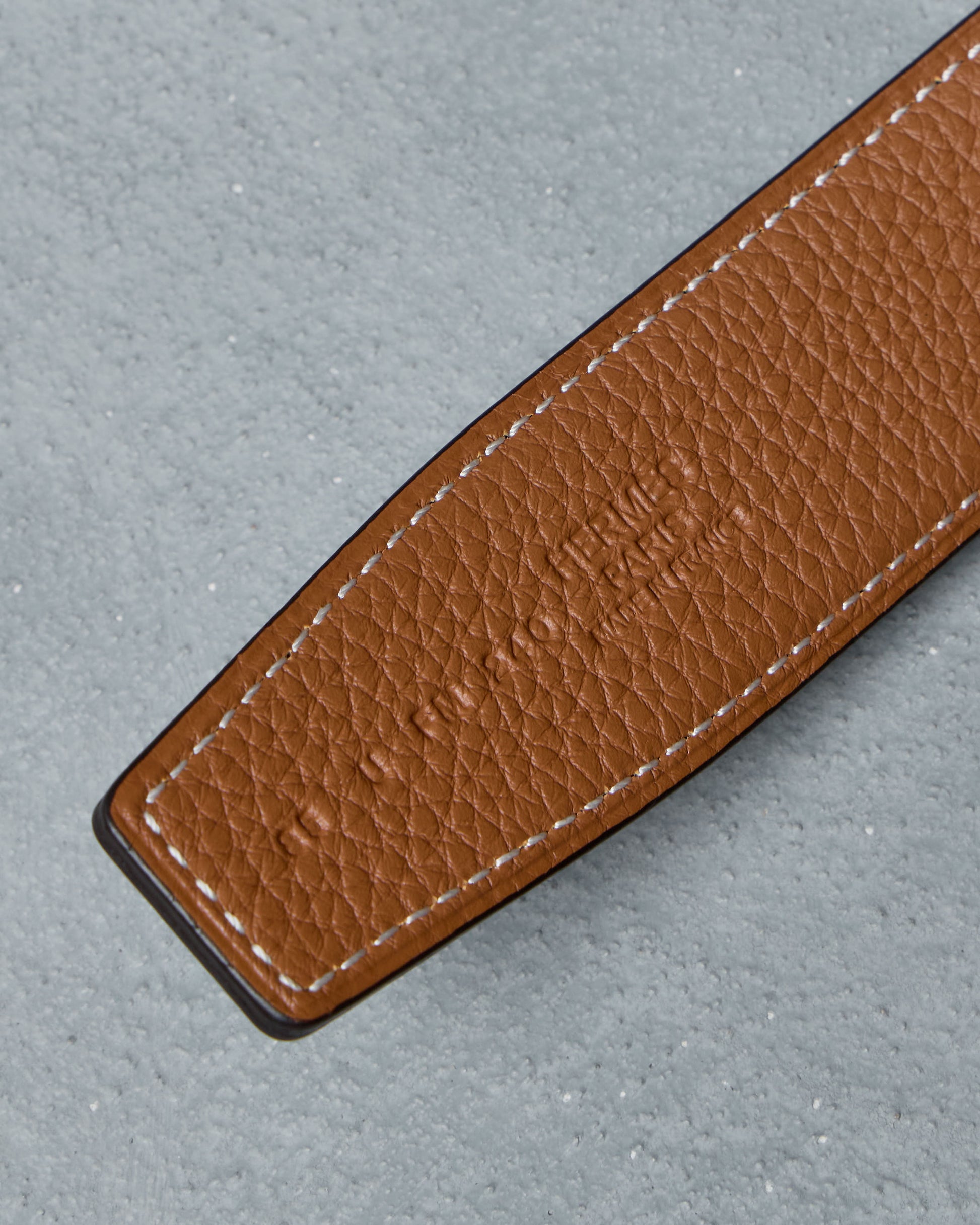Close-up of a brown leather Hermes belt strap on a gray background