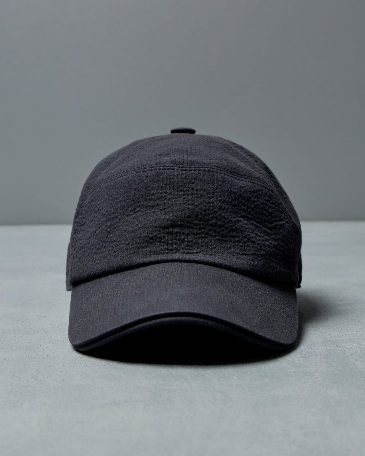 Dark gray Hermès cap on a light gray surface with a gray background