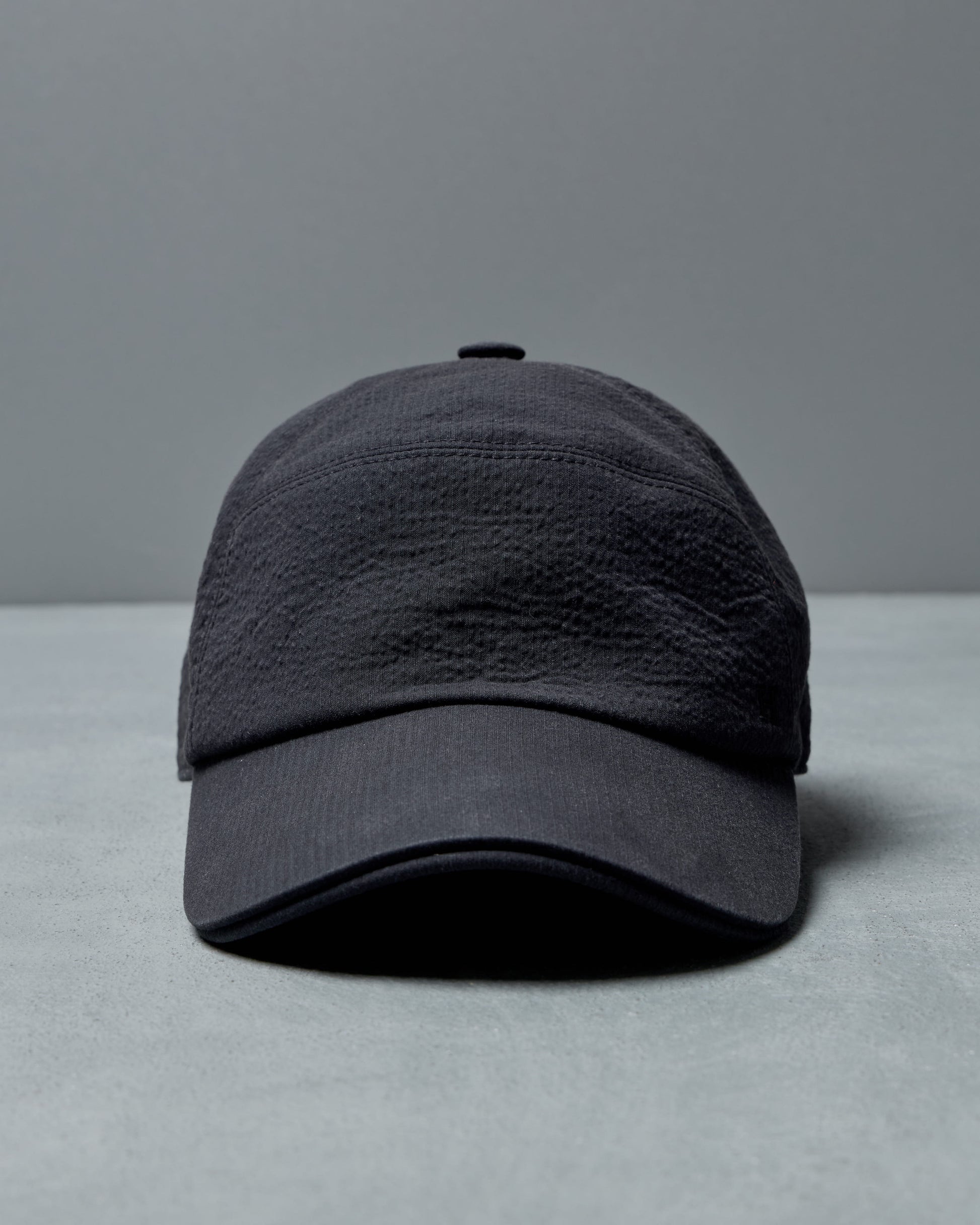 Dark gray Hermès cap on a light gray surface with a gray background