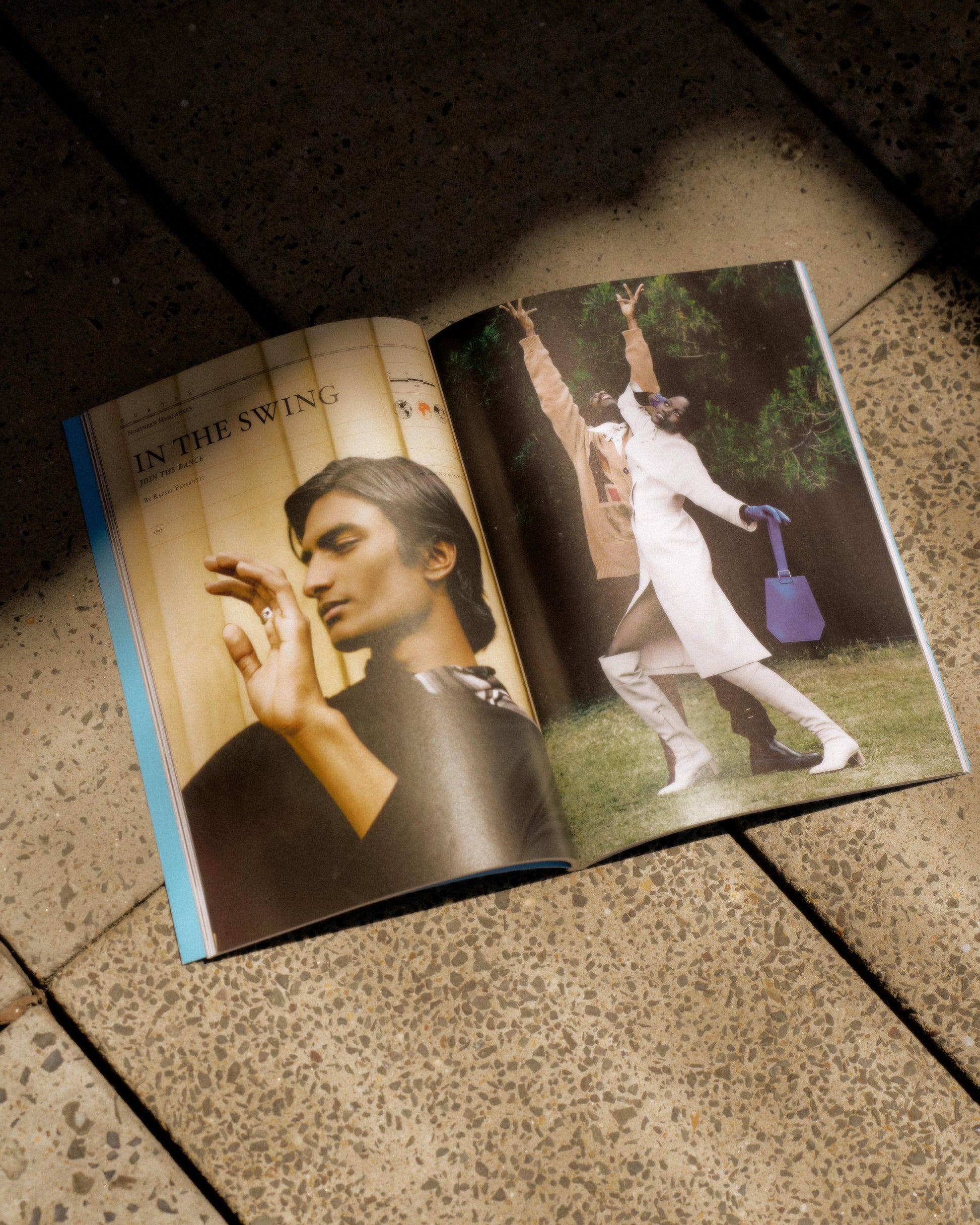 Open Hermes magazine on a tiled floor; left page shows a portrait of a person with closed eyes, right page depicts a person in white, posing energetically outdoors.