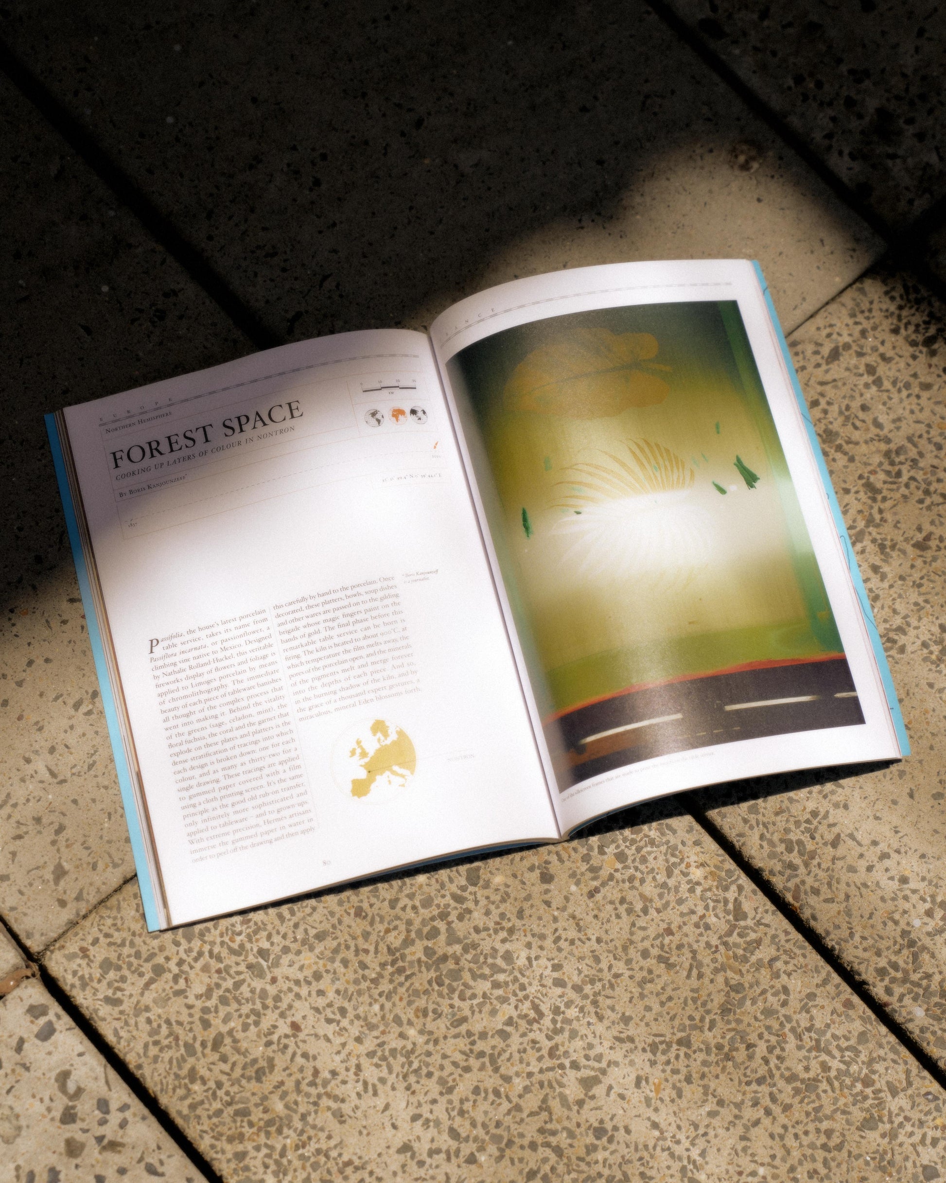 Open Hermes magazine on a tiled floor, featuring an article titled "Forest Space" and an abstract green illustration with curved lines and small tree shapes.