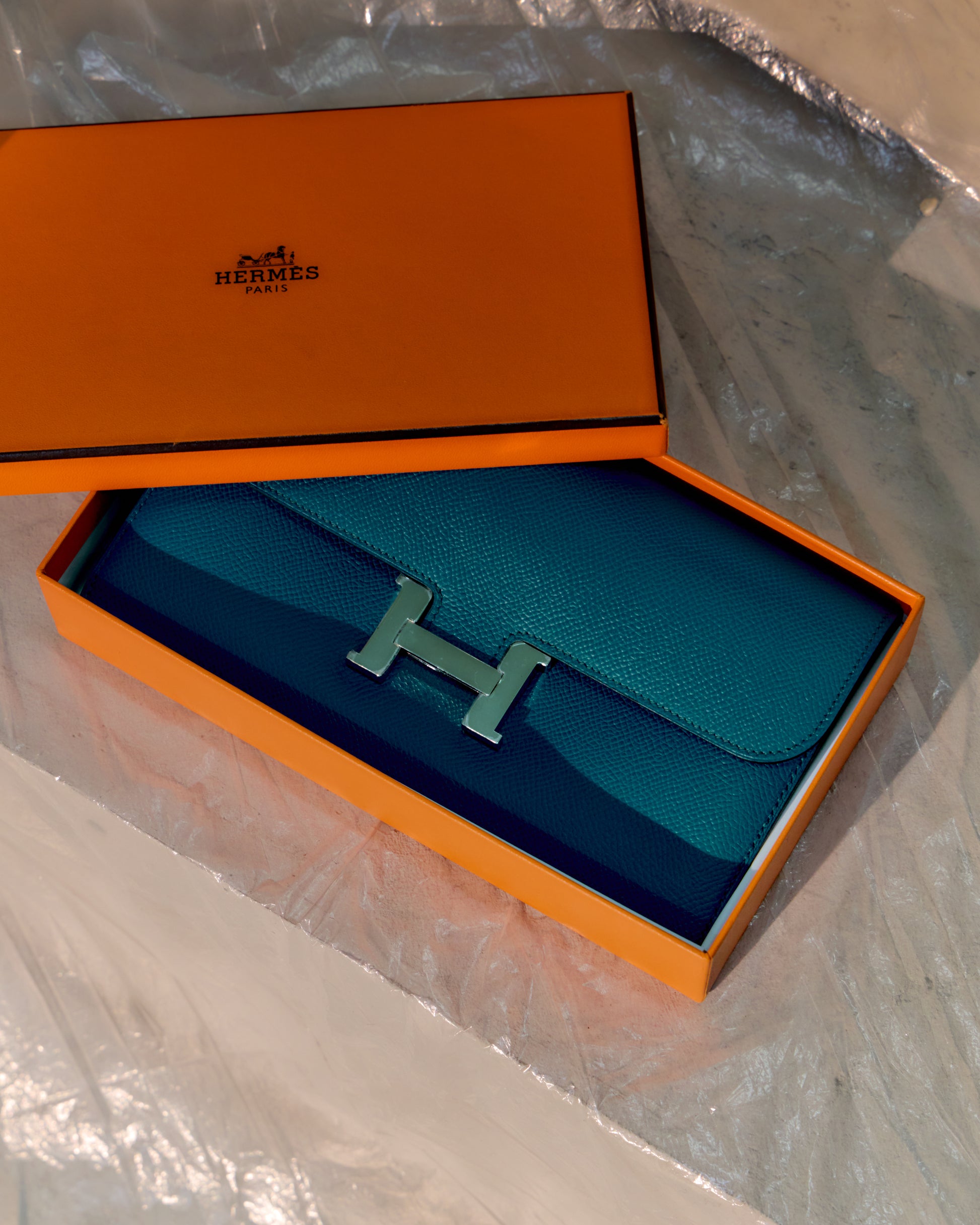 Blue Hermes wallet with orange box on a reflective surface