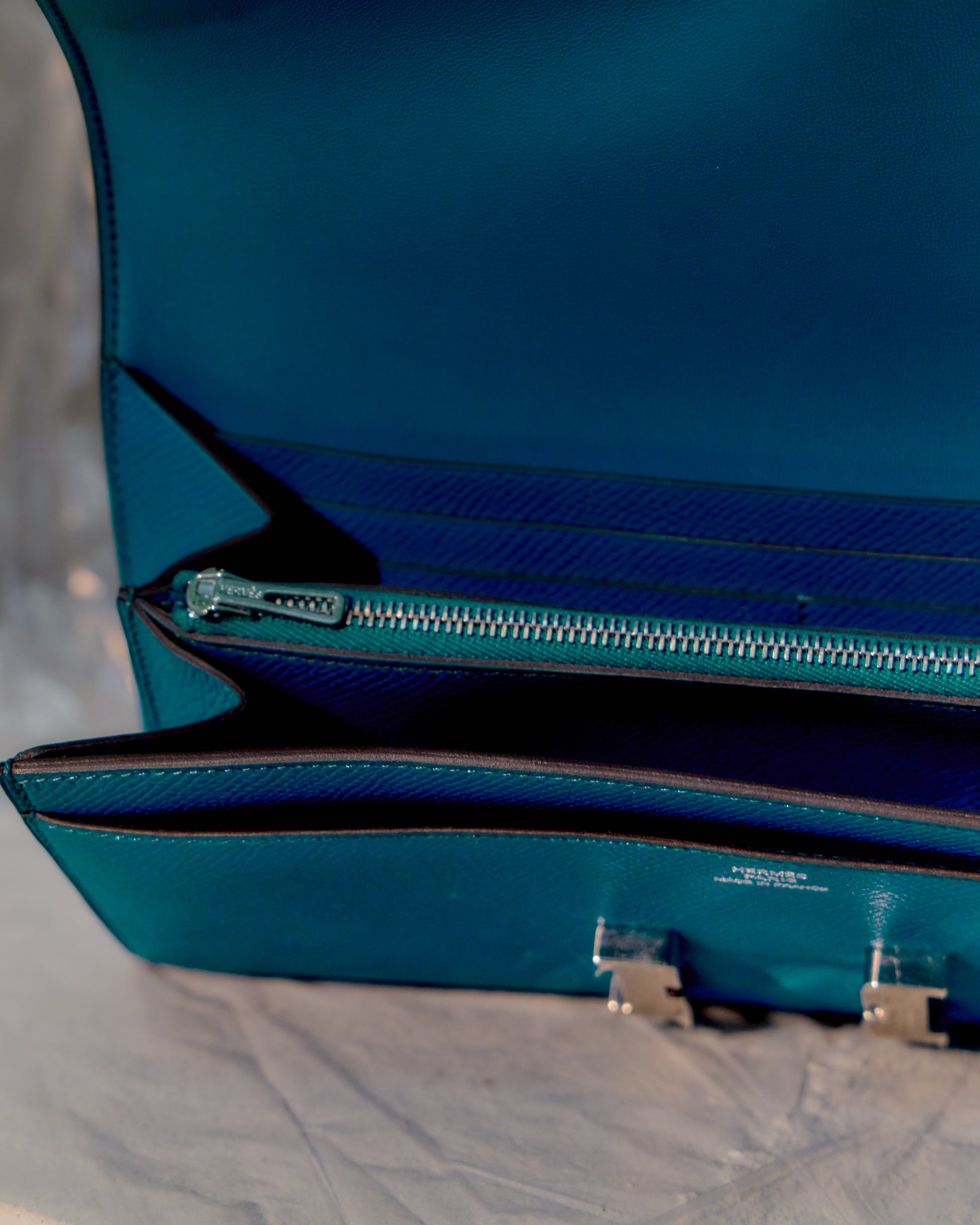 Blue leather Hermès wallet with a visible brand logo on a light grey background