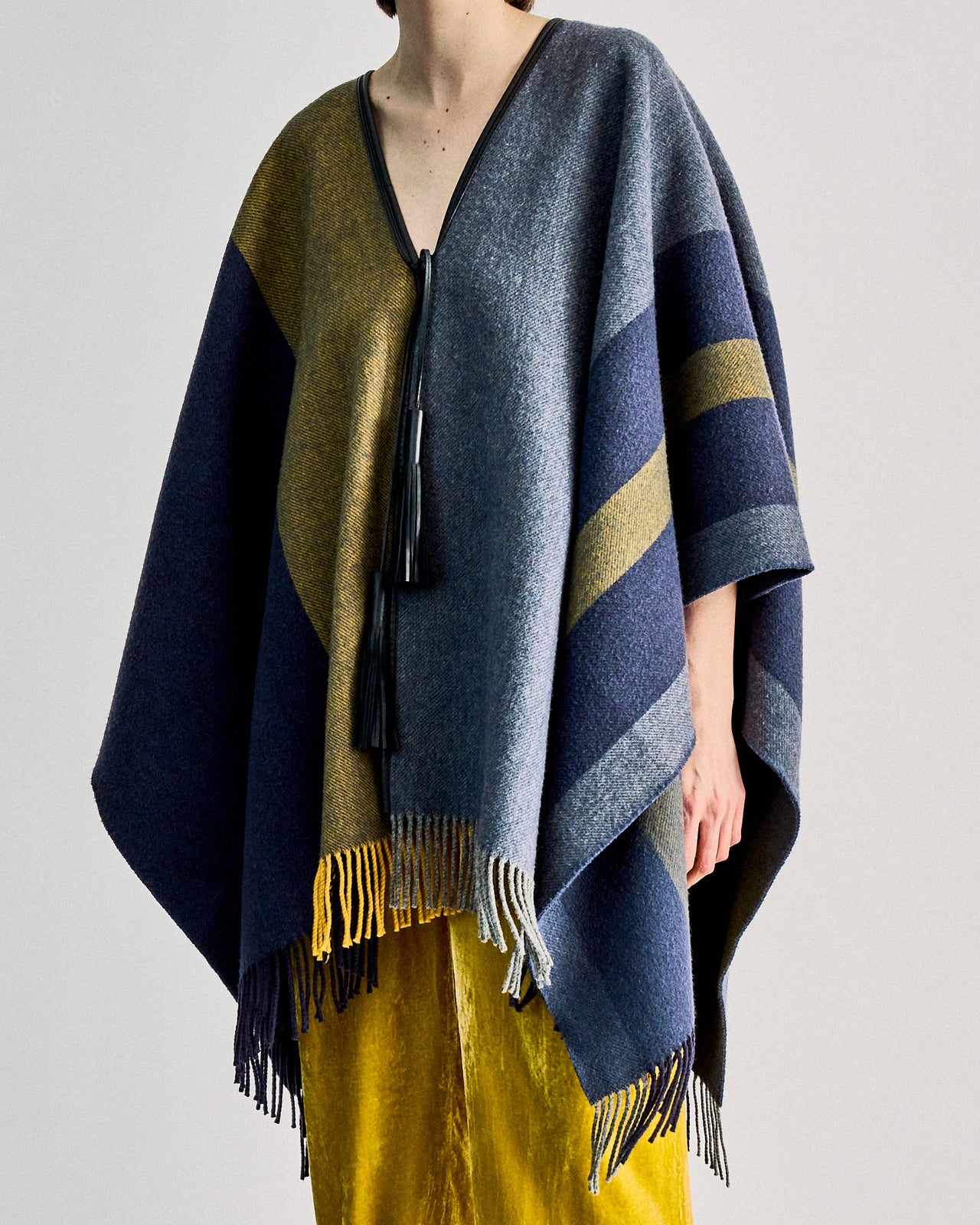 Person wearing a blue and yellow striped Hermès poncho with fringe over yellow pants. 