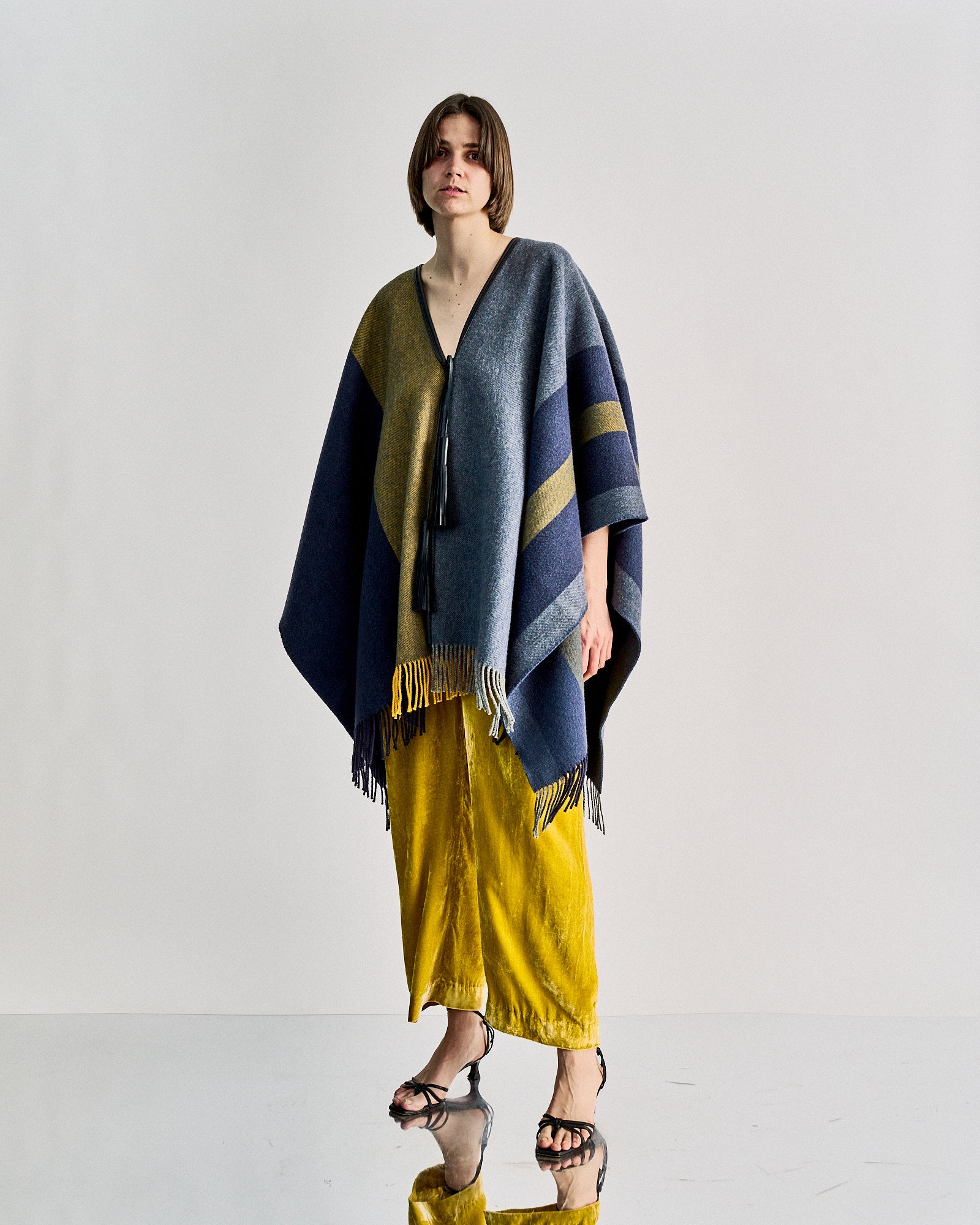 Person wearing a blue and yellow striped Hermès poncho with fringe over yellow pants and black heels.
