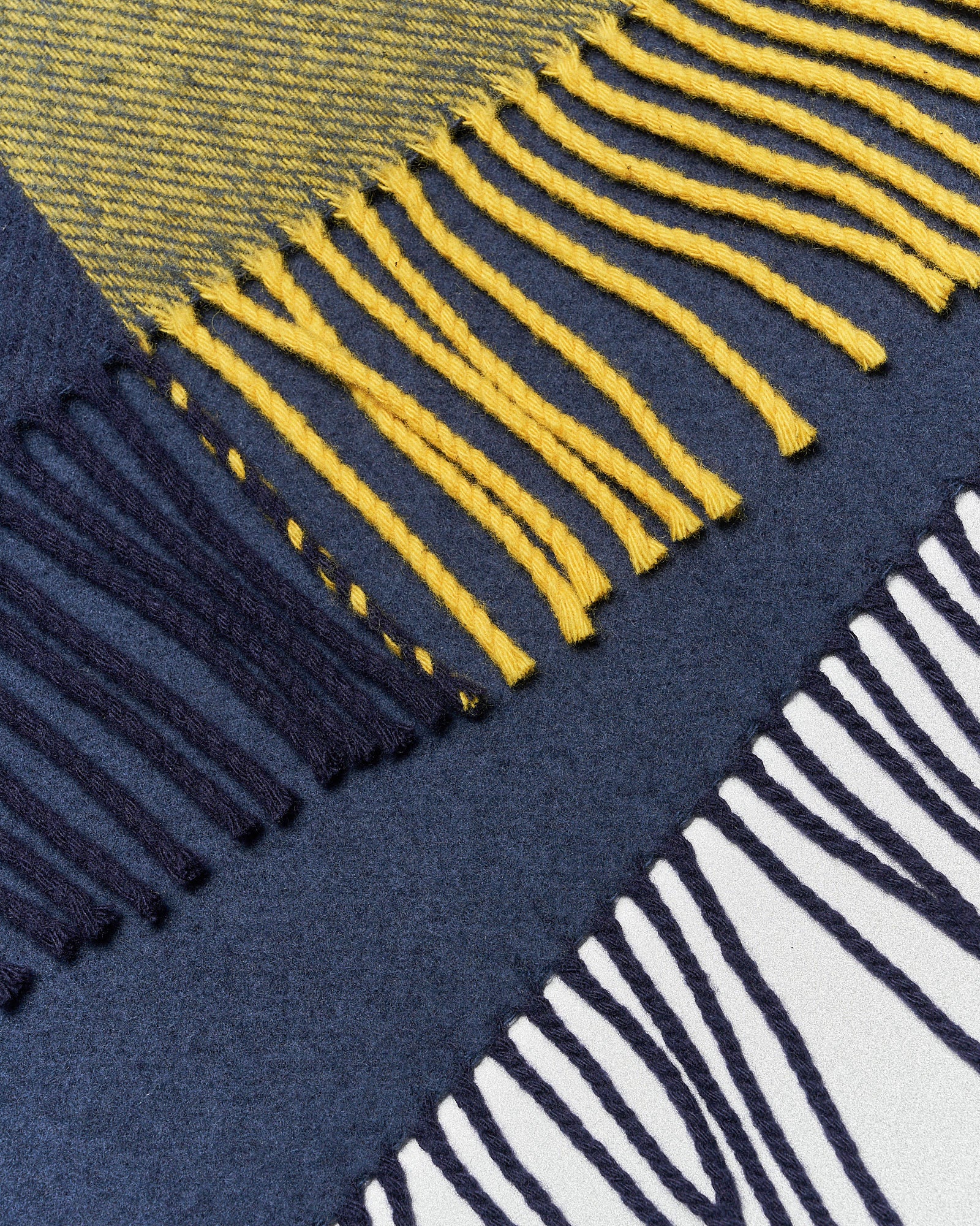 Close-up of three overlapping fringed fabric on a flat surface: one blue and yellow, one dark blue, and one navy and white, creating a textured pattern.