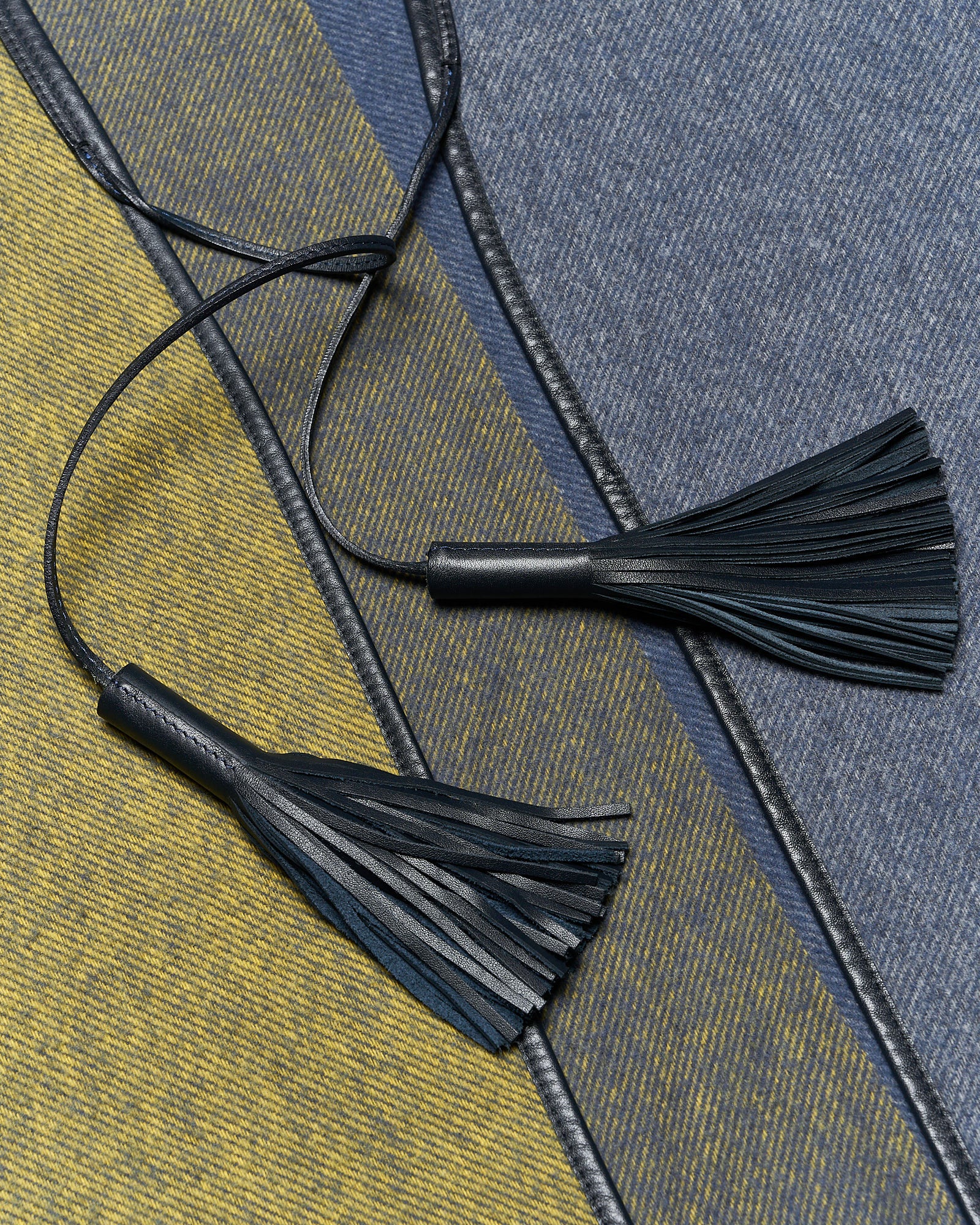 Two dark blue leather tassels rest on diagonally striped denim fabric in blue and yellow shades, creating a textured and stylish contrast.