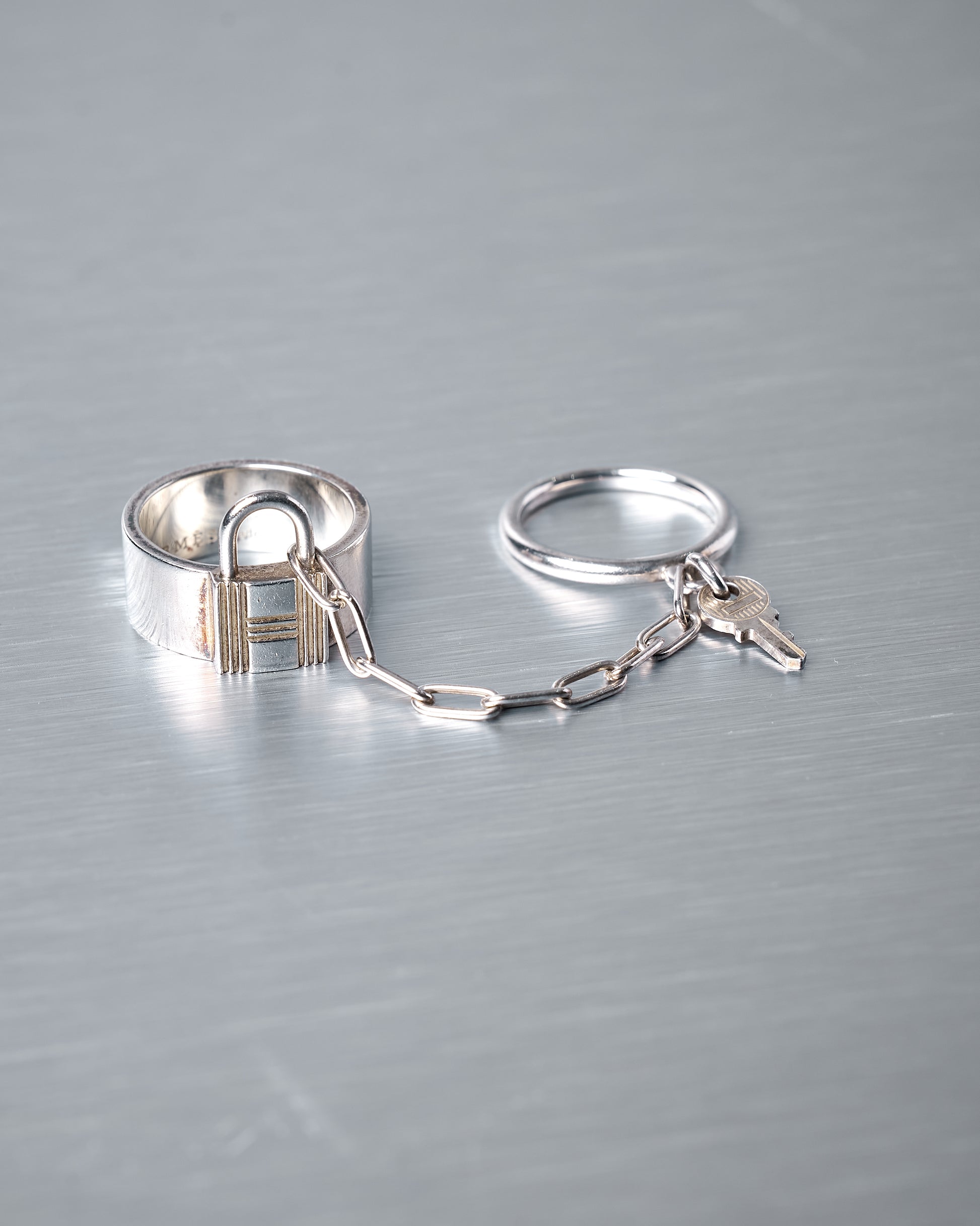 Silver Hermès  key-shaped ring set on a metallic surface