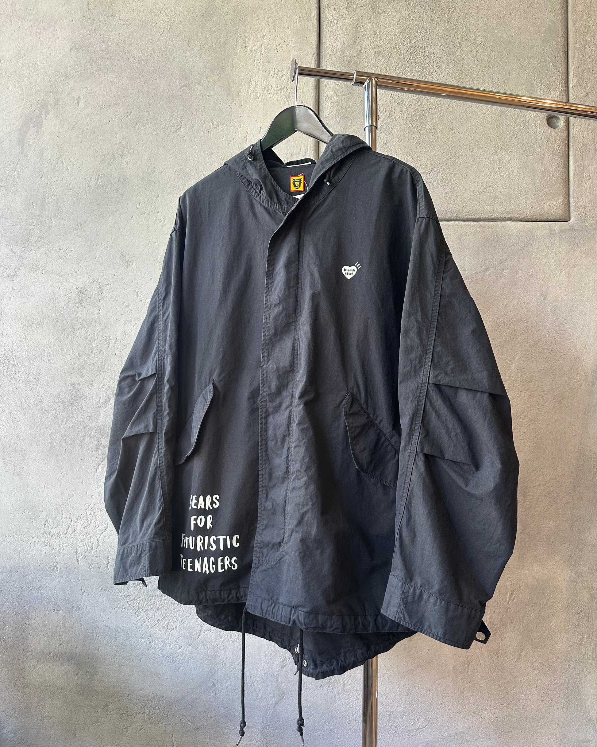 Black Human Made jacket with text on a hanger against a gray wall