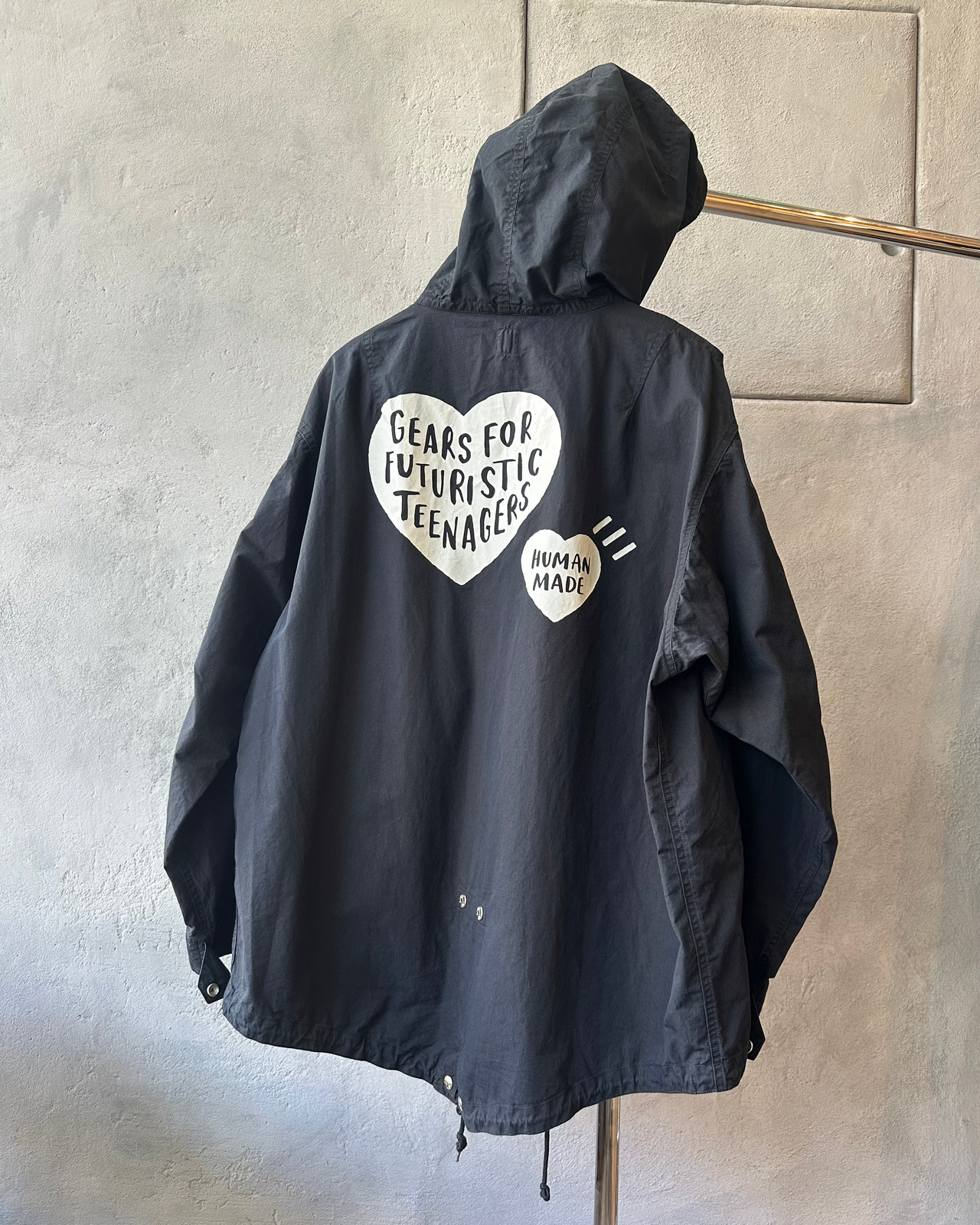 Black Human Made jacket with text on a hanger against a gray wall