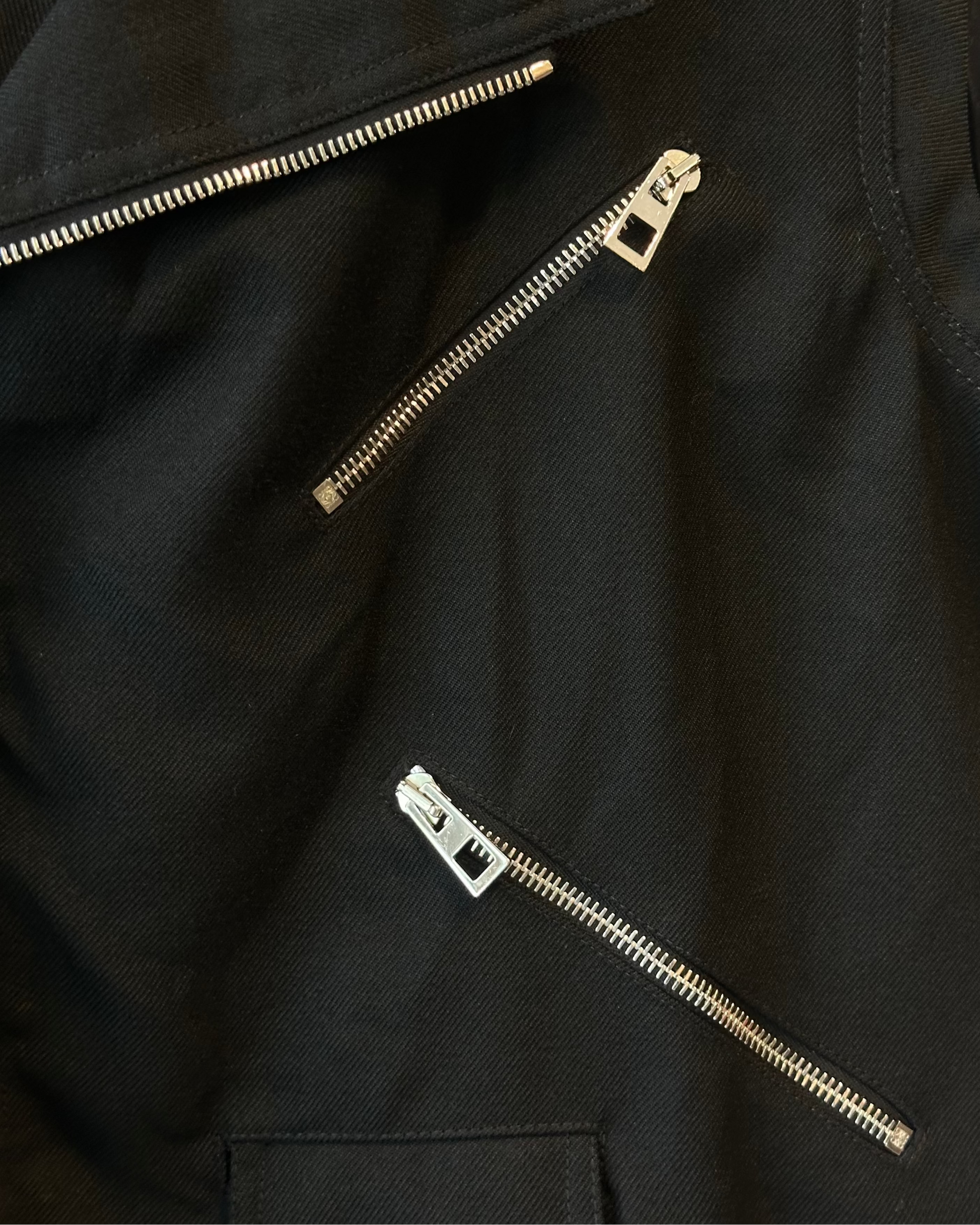 Close-up of a black Loewe jacket with gold zippers on a dark background