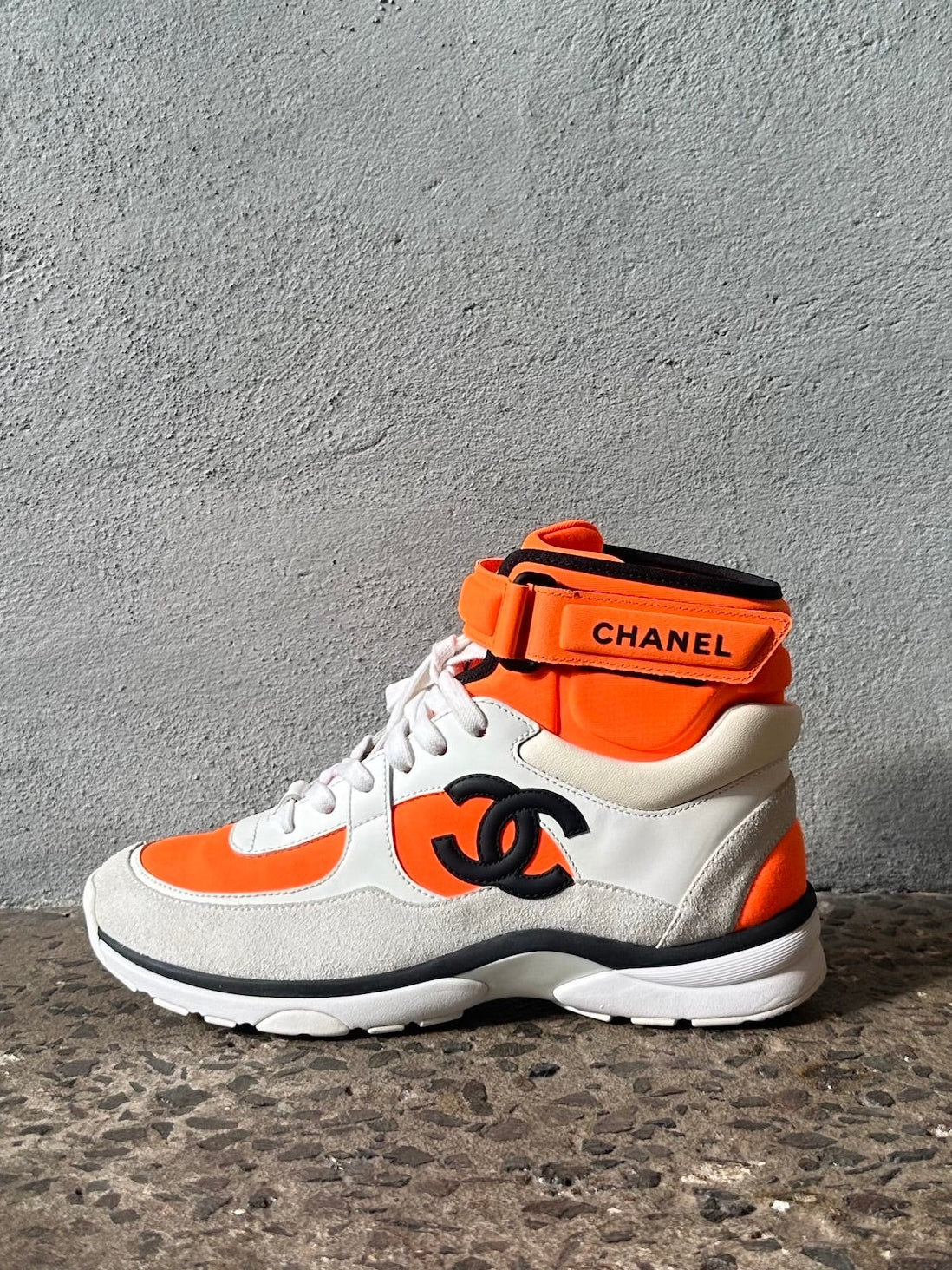 White and orange sneaker with Chanel logo on a gray concrete floor.