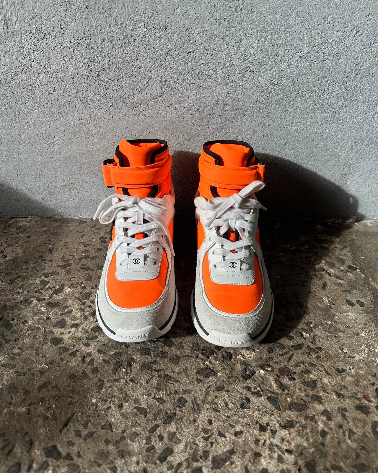 White and orange sneaker with Chanel logo on a gray concrete floor.