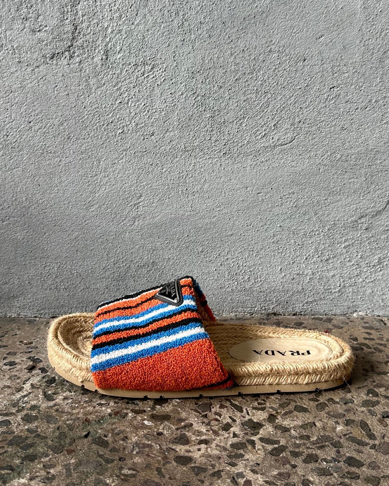 Multicolored sandal with striped pattern on a textured surface against a gray wall.