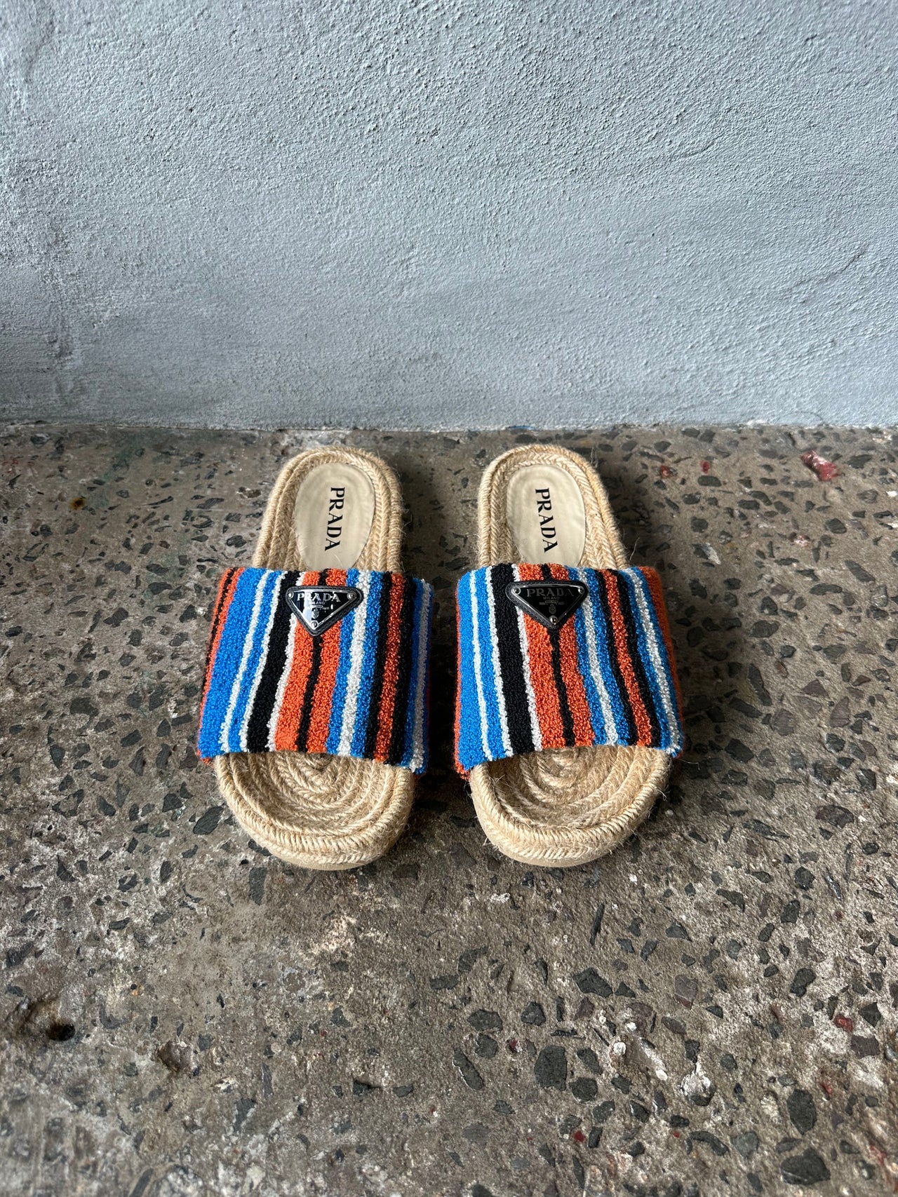 Multicolored sandal with striped pattern on a textured surface against a gray wall.