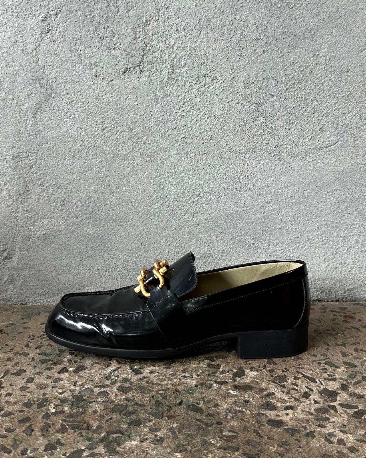 Black loafer shoe on a textured concrete floor against a gray wall