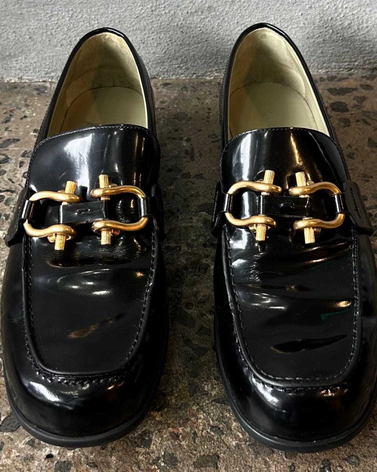 Black loafer shoe on a textured concrete floor against a gray wall