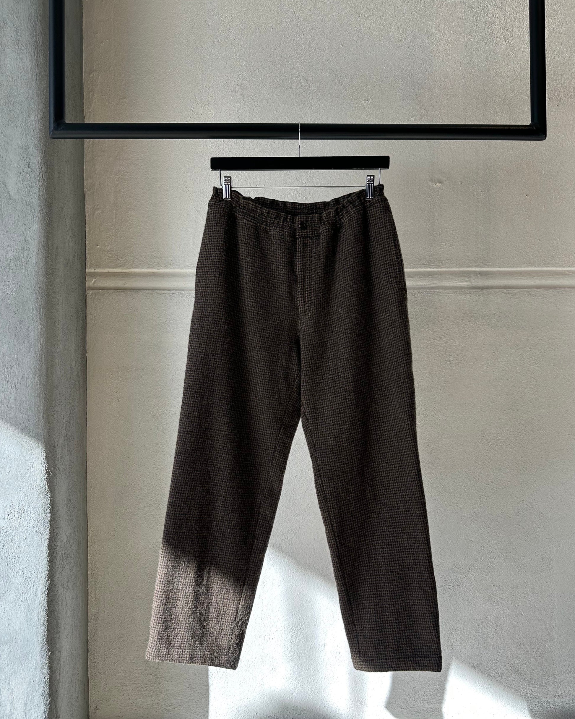 Dark gray pants hanging on a rack against a light-colored wall.