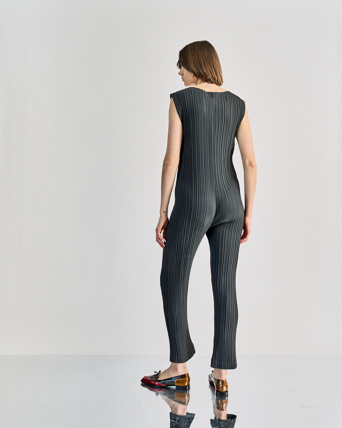 A model wearing an Issey Miyake 1980's Pleated V-neck jumpsuit in black, featuring a deep V-neck and flat box pleats.